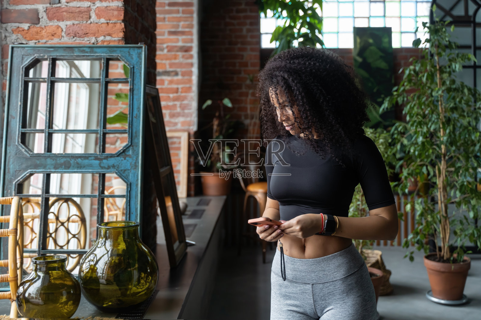 留着非洲卷发的黑人女性在家里或室内咖啡馆使用智能手机。与亲戚朋友交流。社交媒体。视频图片内容。舒适的关系。自由照片摄影图片