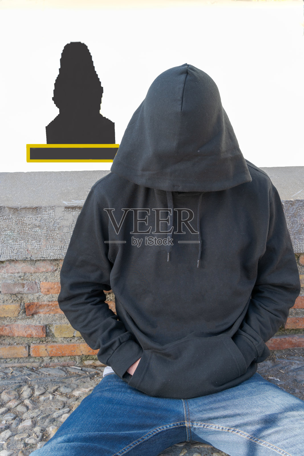 坐着的男人穿着黑色连帽运动衫，遮住了他的脸和牛仔裤。照片摄影图片