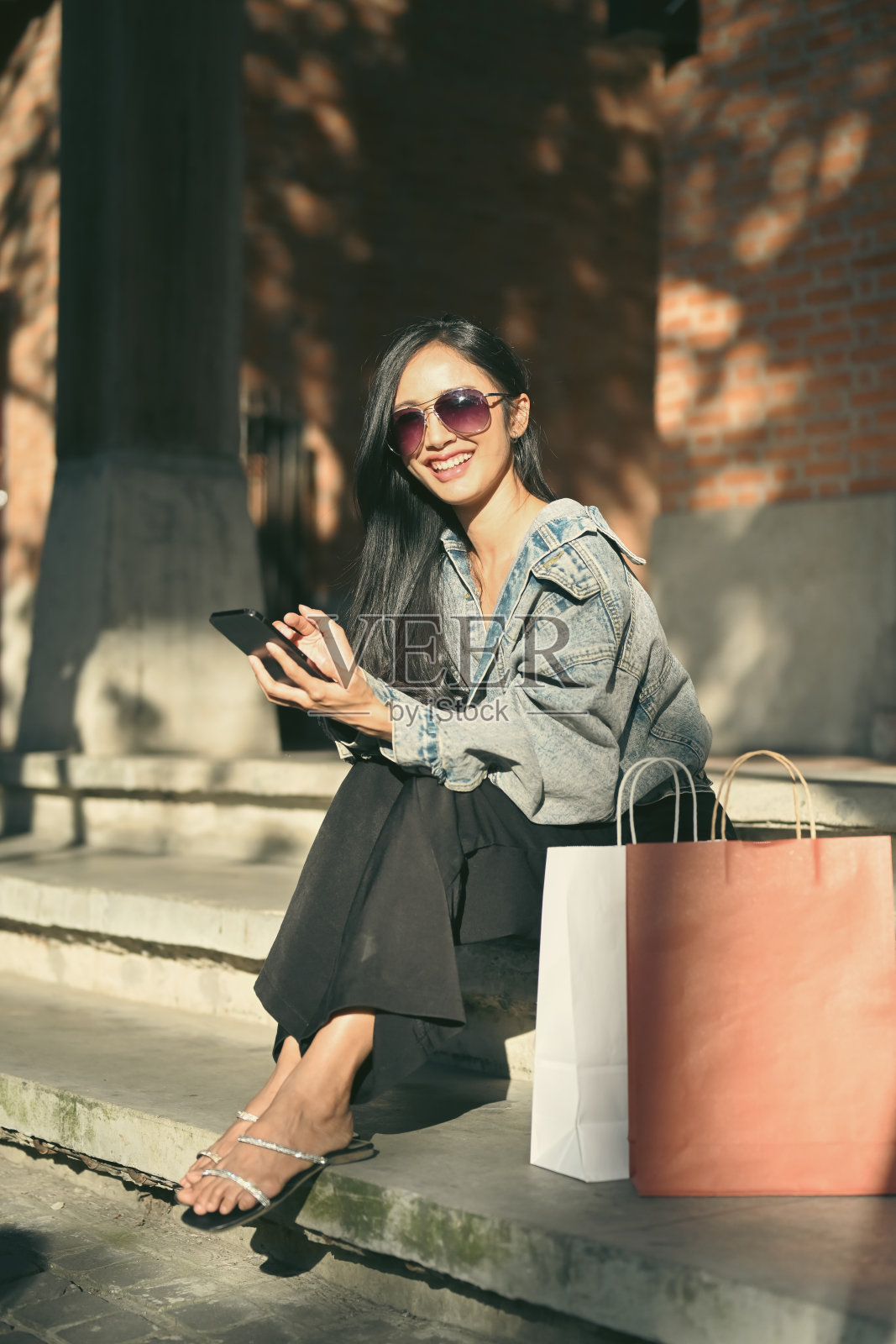 千禧一代女性的肖像，穿着时髦的衣服，戴着太阳镜，坐在城市购物区的楼梯上。照片摄影图片