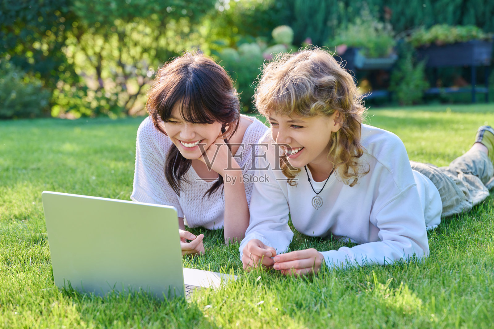 十几岁的女学生朋友笑着躺在草地上用笔记本电脑照片摄影图片