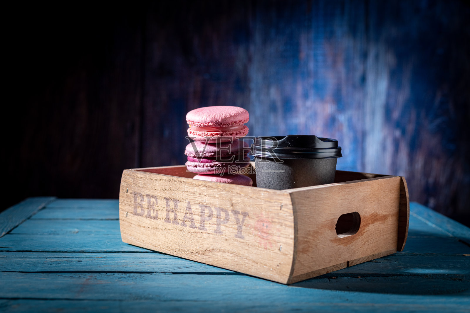 马卡龙和咖啡放在木托盘里。五彩的蛋白杏仁饼和装在木盒里的咖啡。彩色背景。照片摄影图片