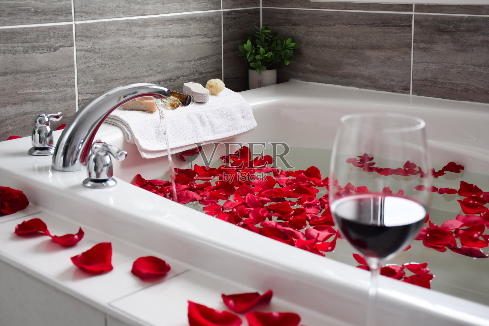 在浴缸边放一杯红酒，洒上红色的玫瑰花瓣照片摄影图片