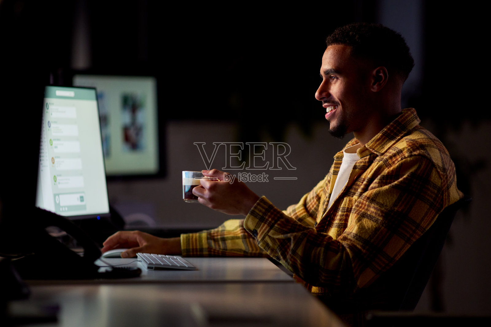 商人在办公室工作到很晚，喝咖啡时被电脑屏幕照亮了脸照片摄影图片