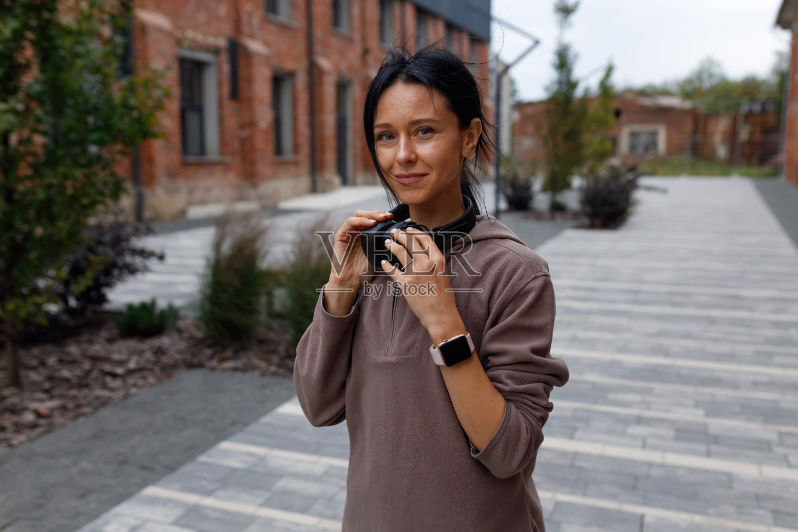 迷人的运动女性与无线耳机在她的脖子站在户外照片摄影图片