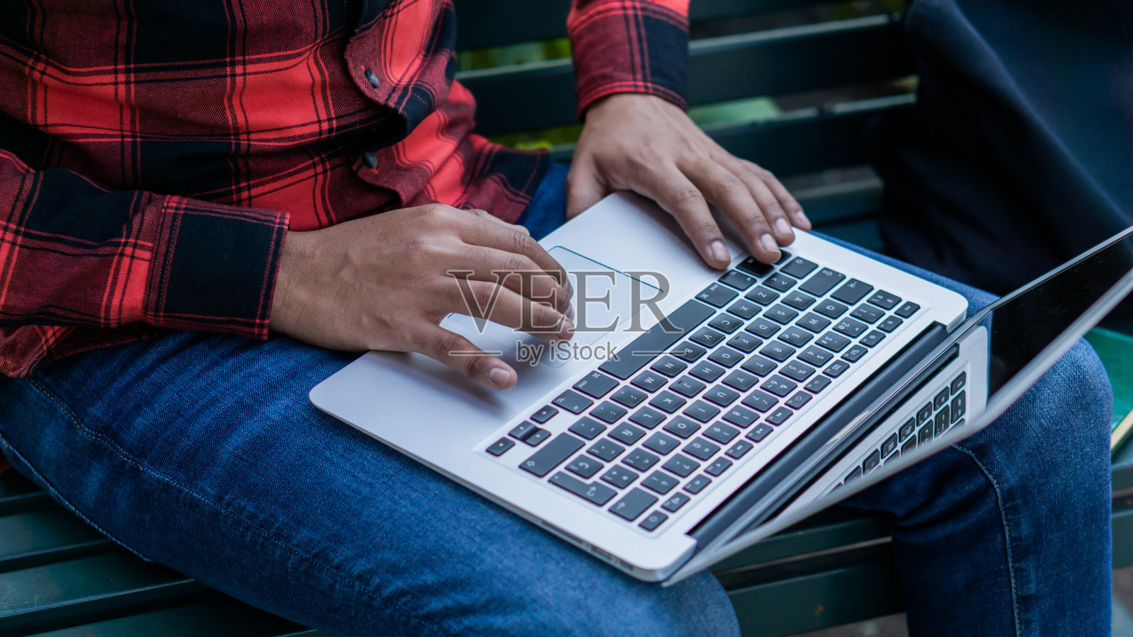 一个棕色皮肤的人在外面的电脑上打字的手。照片摄影图片