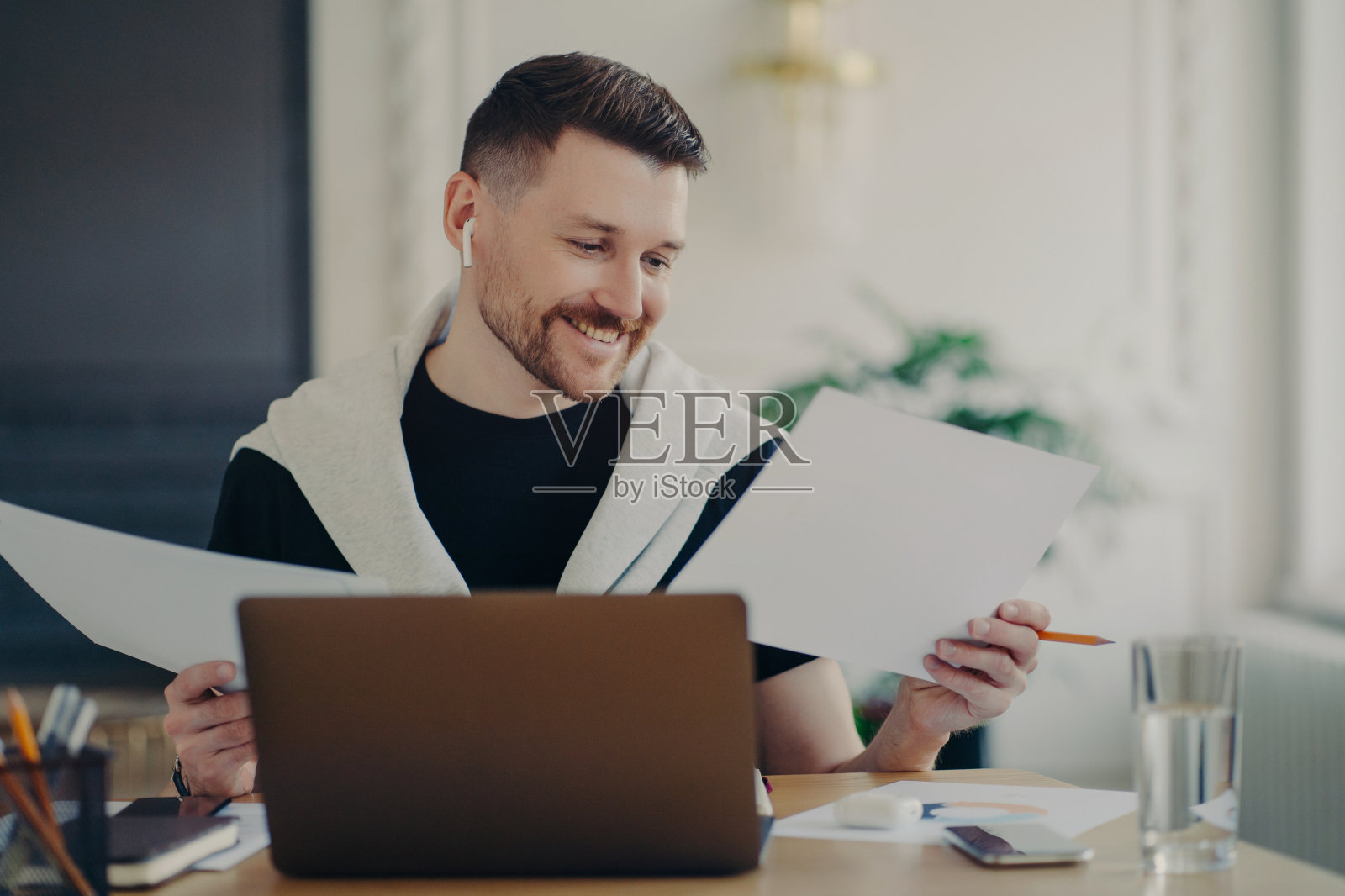 英俊快乐的商人分析文件和感觉满意，而工作在笔记本电脑从家里照片摄影图片