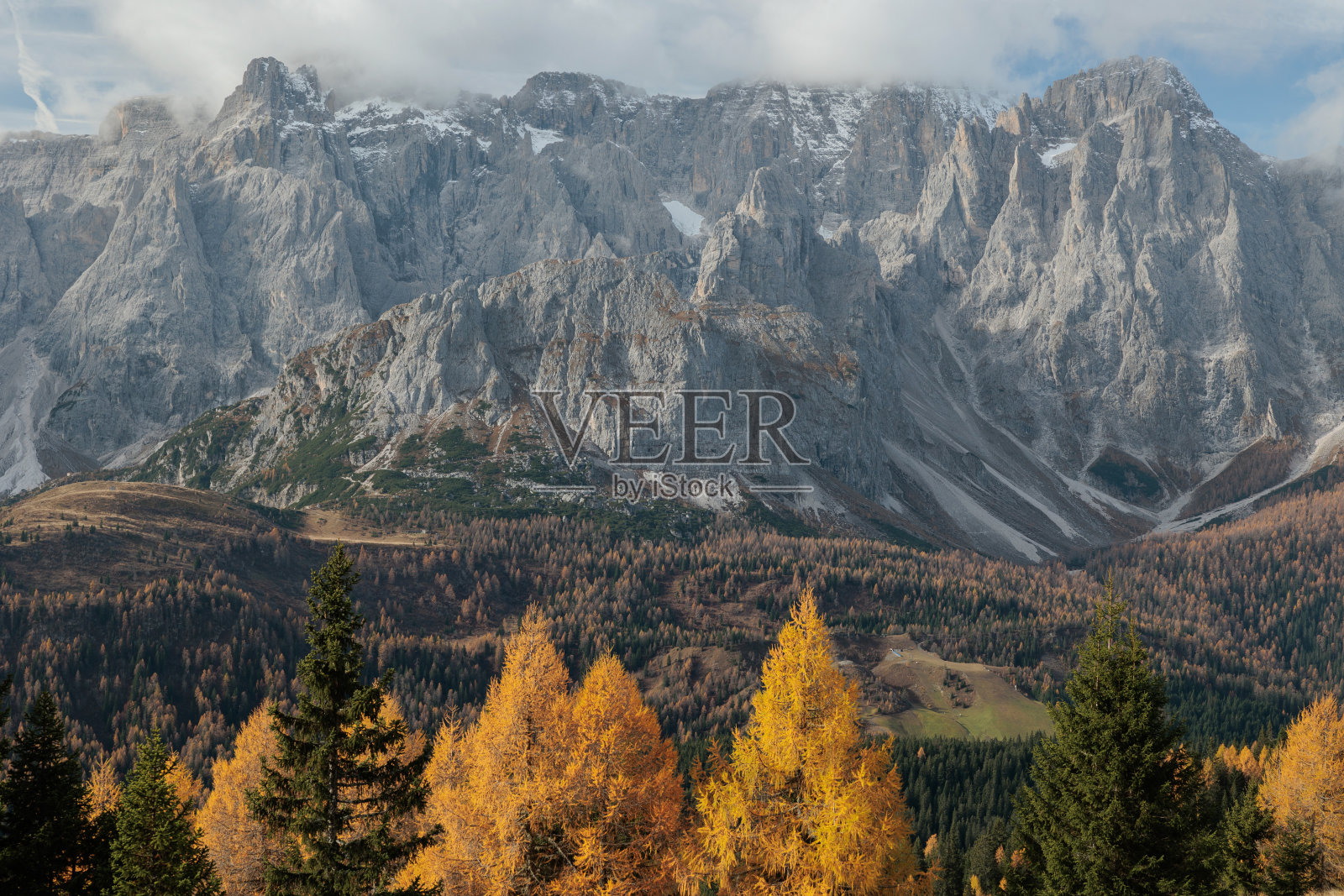 近距离观看西玛昂迪奇山的山脊，在底部被五颜六色的针叶林包围。轻云在山峰上飞翔照片摄影图片
