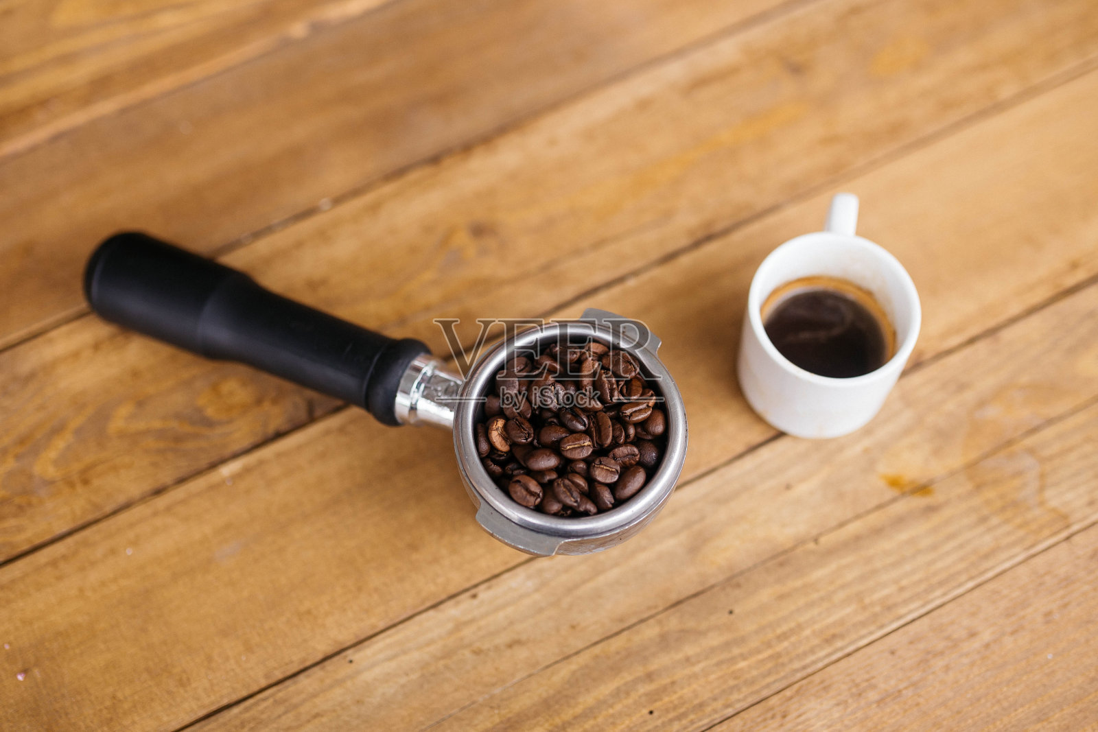 俯视图咖啡豆在无底过滤器与黑咖啡杯在木桌上，选择性聚焦。咖啡豆放在木桌上的无底过滤器里。照片摄影图片