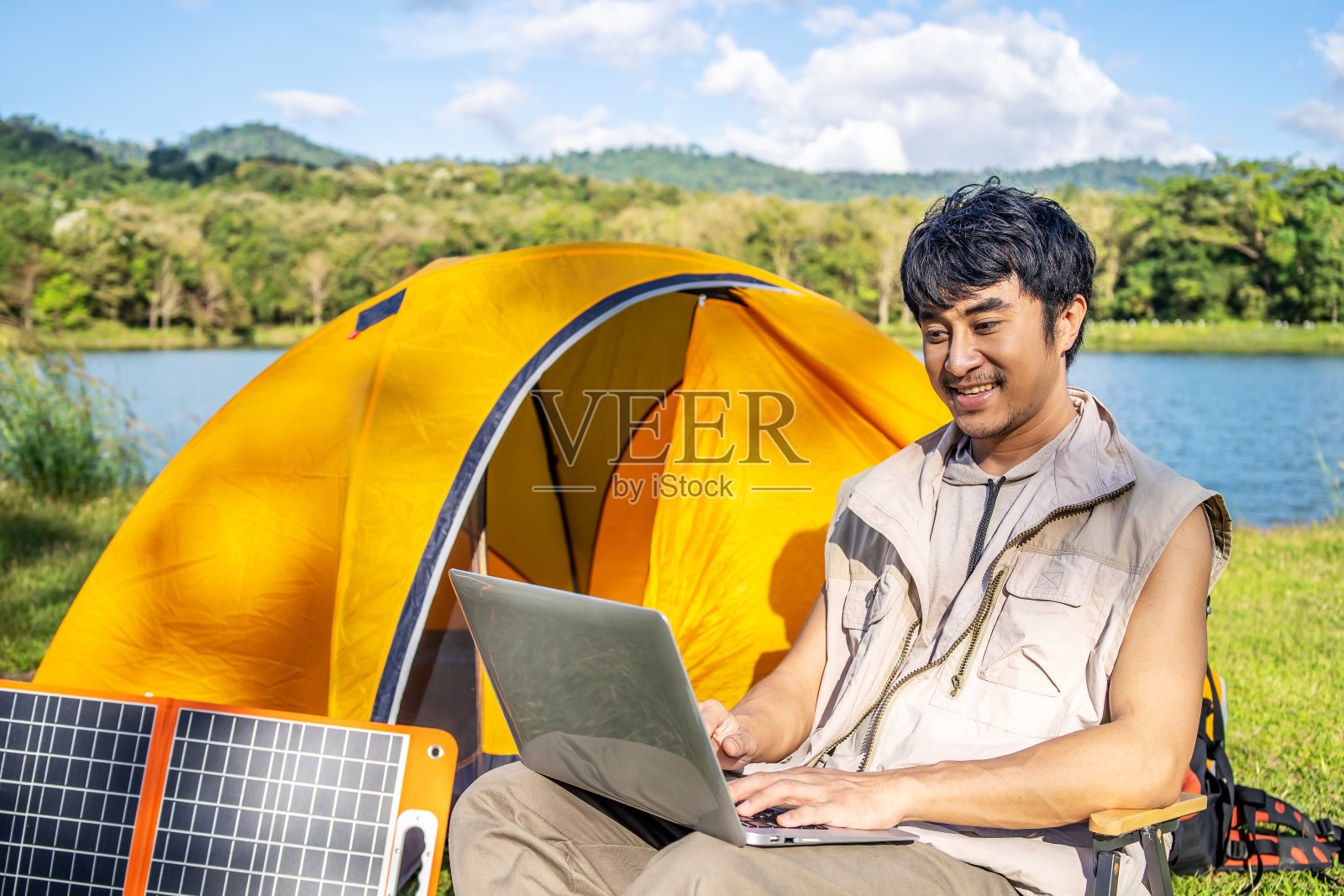 年轻的亚洲旅行家在暑假放松和享受户外露营的生活方式。有吸引力的男性在椅子上放松，在大自然的露营日在笔记本电脑上工作照片摄影图片