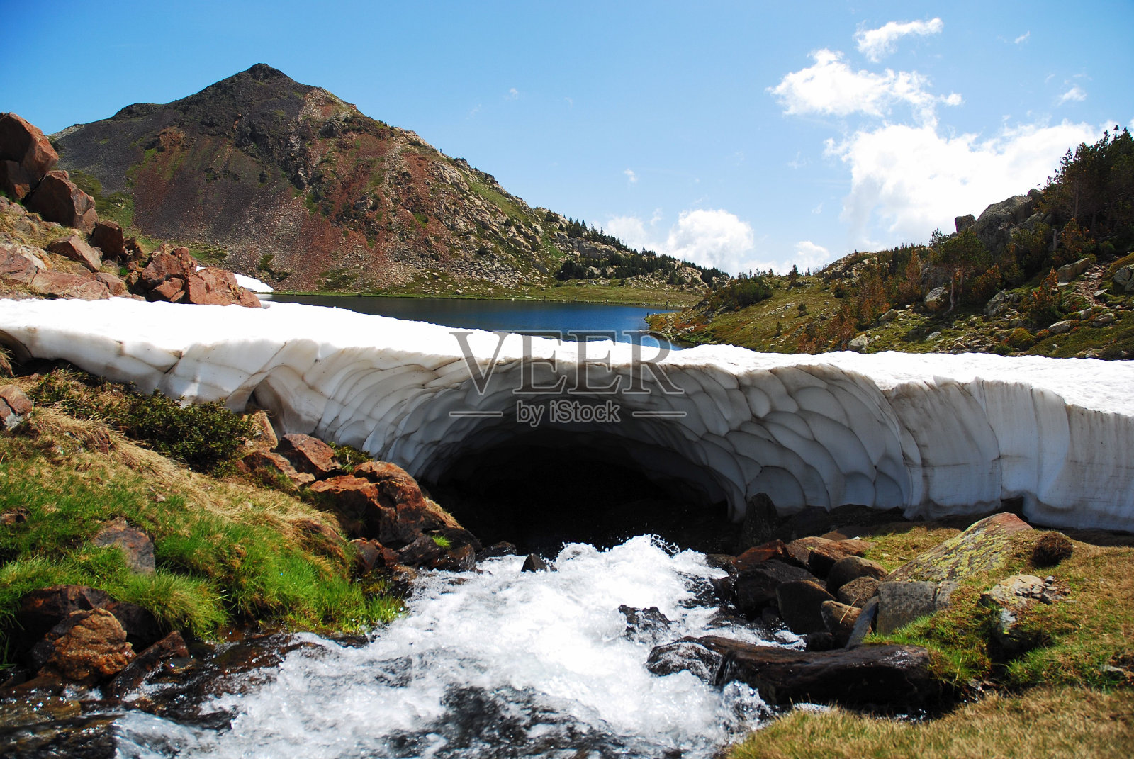 河流在冰拱下流动，背景是山脉之间的湖泊照片摄影图片