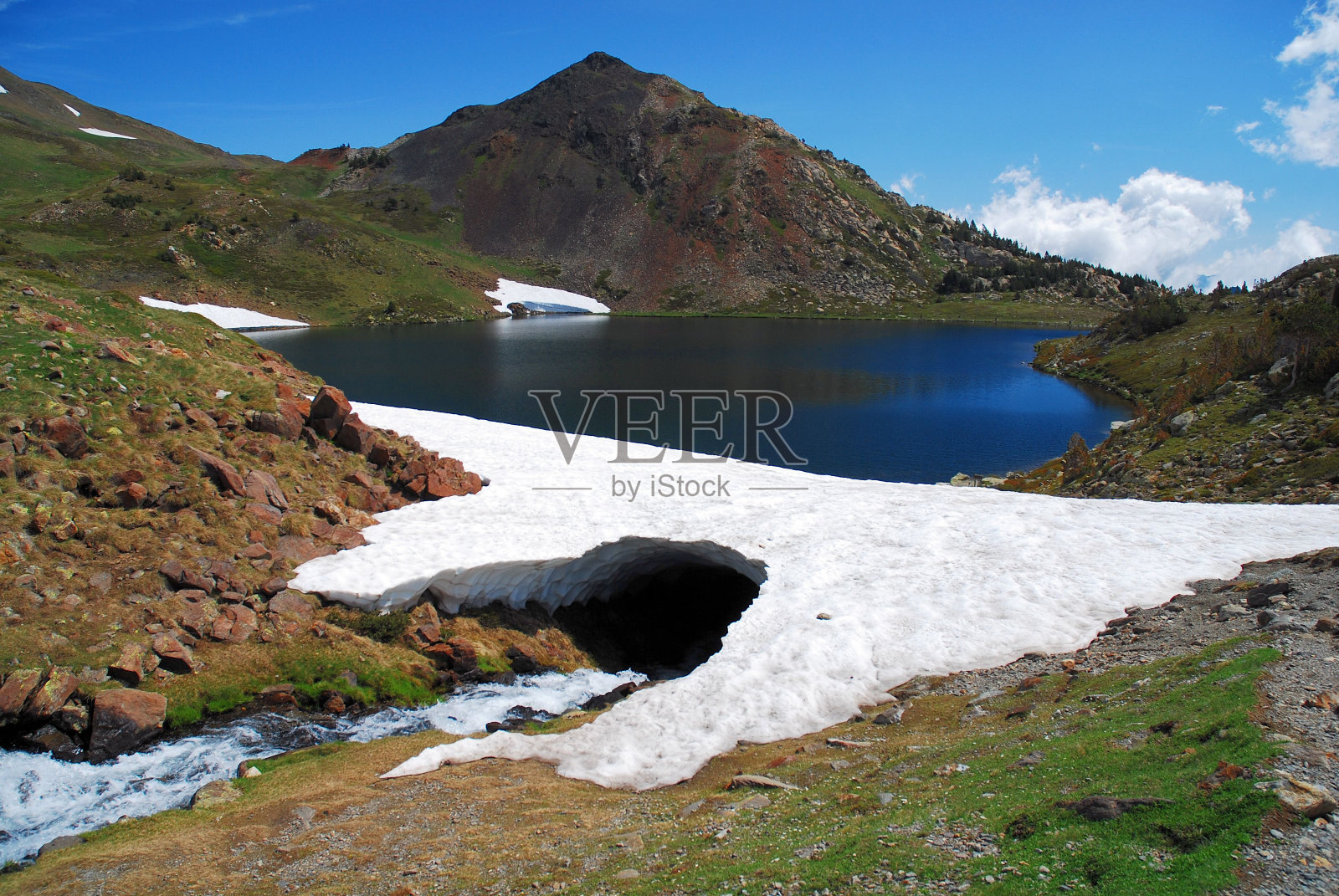河流在冰拱下流动，背景是山脉之间的湖泊照片摄影图片