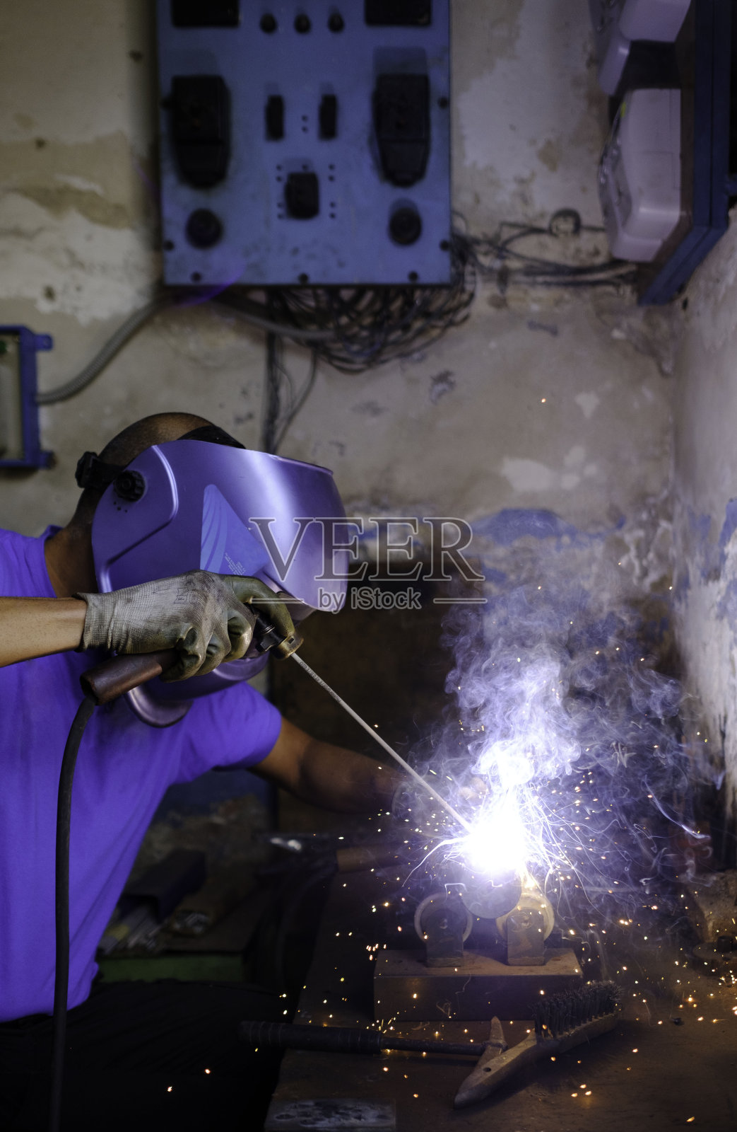 家庭车间，戴着焊接手套和面罩，在焊机旁工作的金属工人。熟练的劳动力。照片摄影图片
