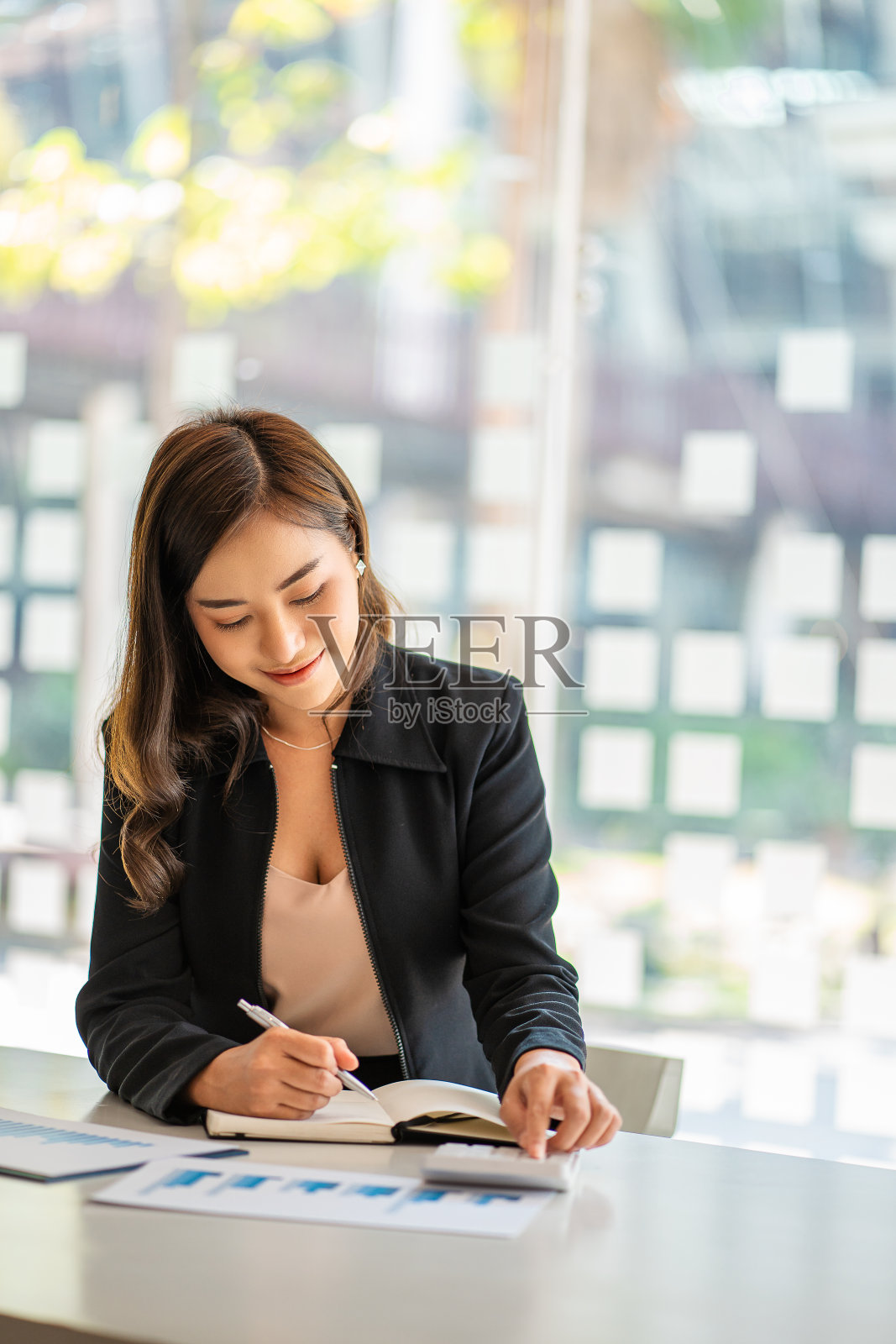 微笑的亚洲商人在纸上工作，拿着笔和笔记本电脑坐在现代家庭工作室的椅子上。流动工人在工作和计算器财务或会计概念照片摄影图片