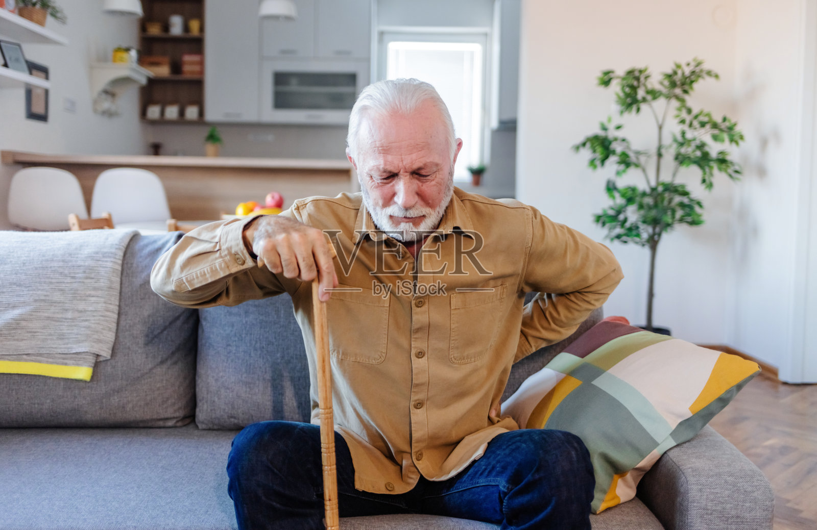 一位身患残疾的大胡子老人独自一人在家里挣扎着起床，脸上露出了悲伤和绝望的表情。照片摄影图片