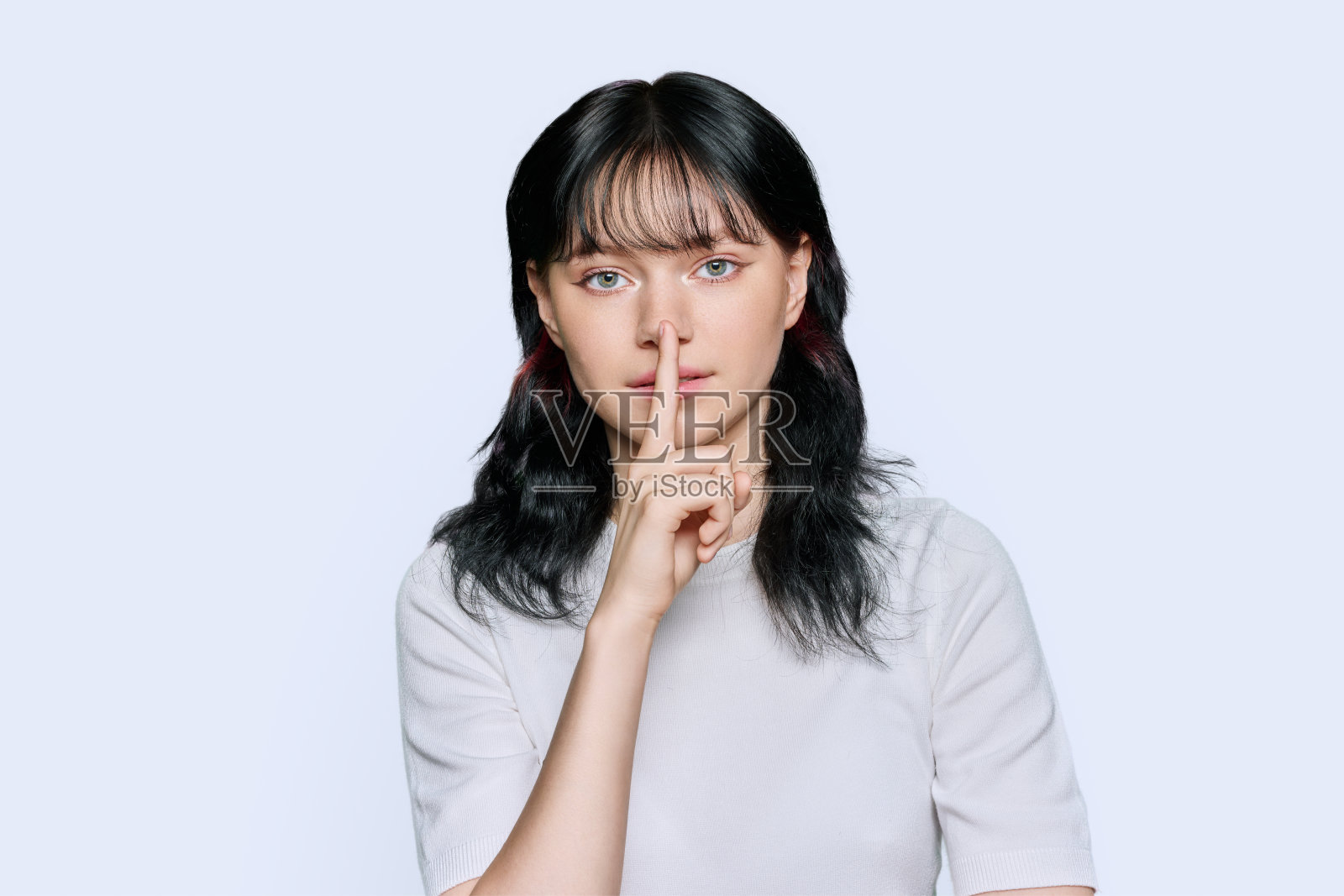 年轻女子显示沉默的手势，手指在嘴唇上，白色背景照片摄影图片