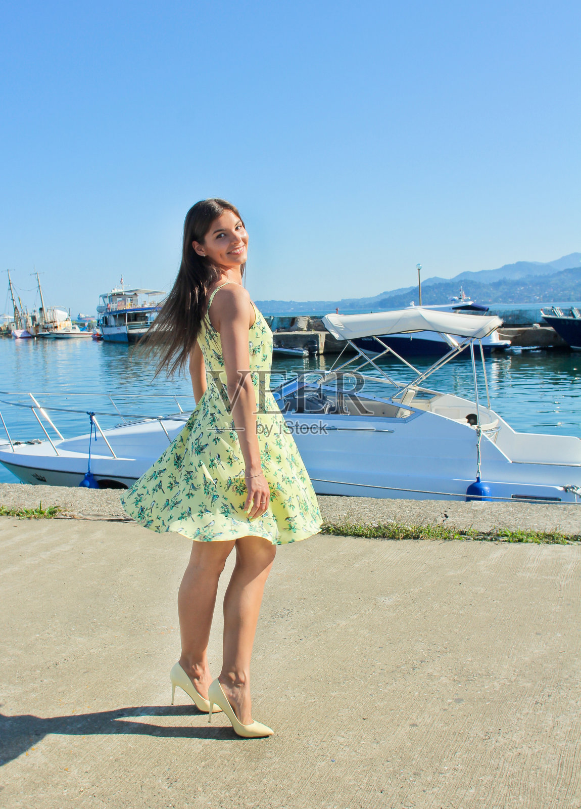 漂亮的黑发年轻女子穿着黄色连衣裙在街上跳舞，靠近海港。照片摄影图片