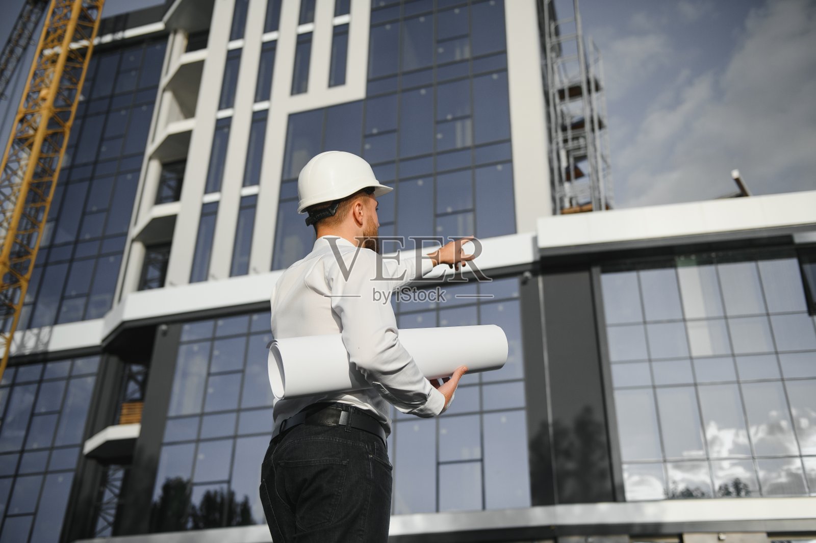 工程师在起重机旁边。概念-大型建设项目。建筑师指导施工过程。手里有图纸和写字板。照片摄影图片