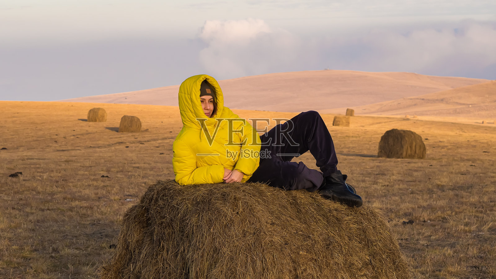 一个穿着温暖的黄色夹克的女人躺在田野里的干草堆上。白种人的农村照片摄影图片