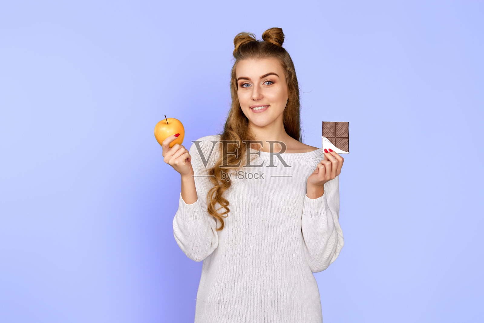 穿着毛衣的女人展示了甜美的巧克力棒和新鲜的苹果照片摄影图片