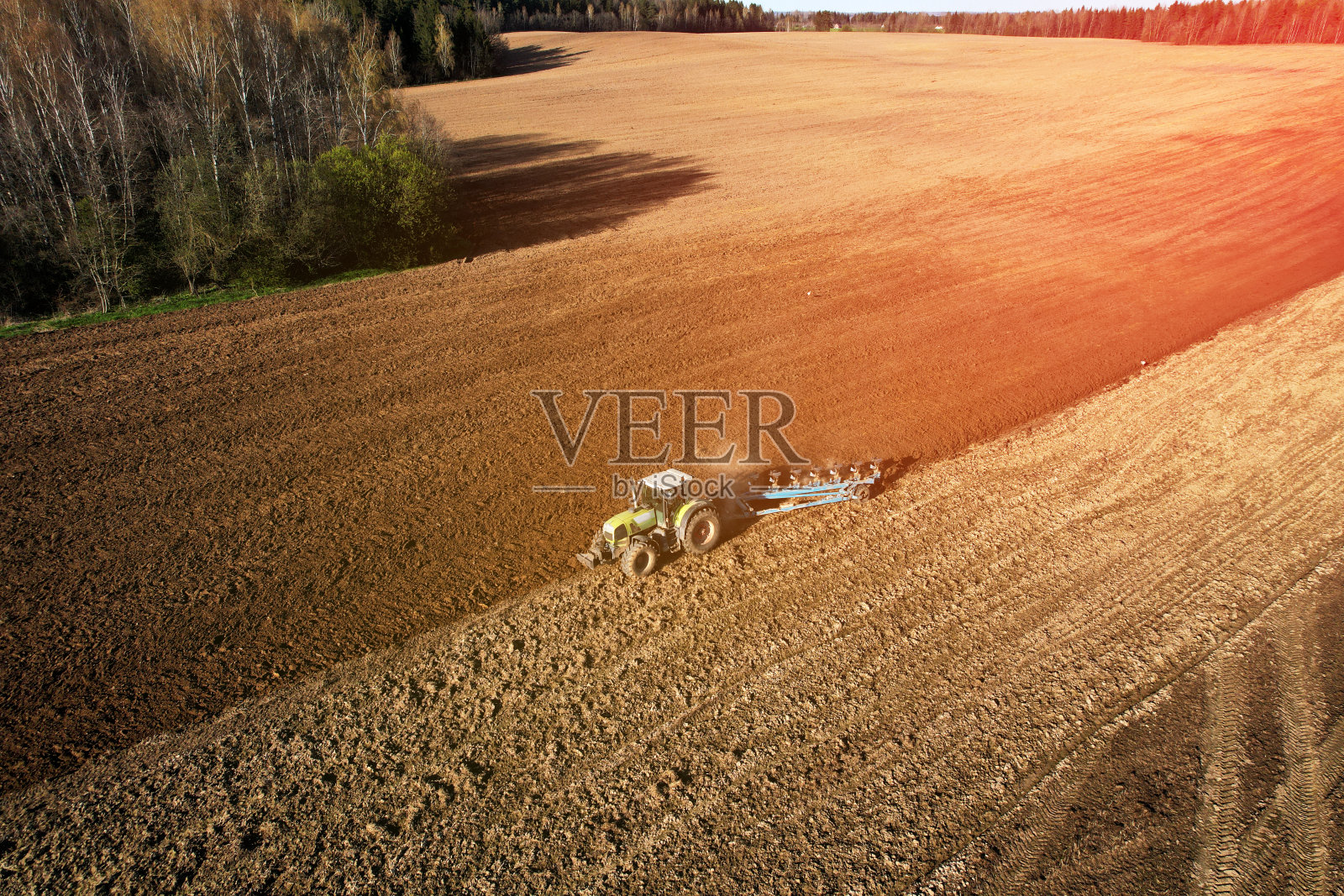 拖拉机带犁在田间耕作。绿色拖拉机在夕阳下犁地。照片摄影图片