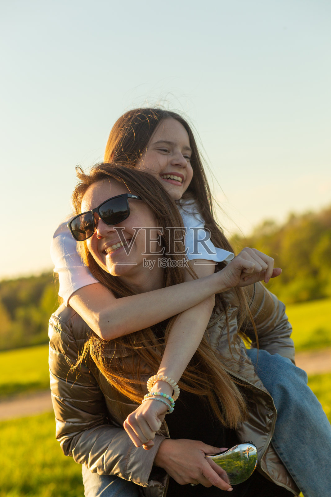 顽皮的母亲给女儿小猪背骑在绿色的田野。照片摄影图片