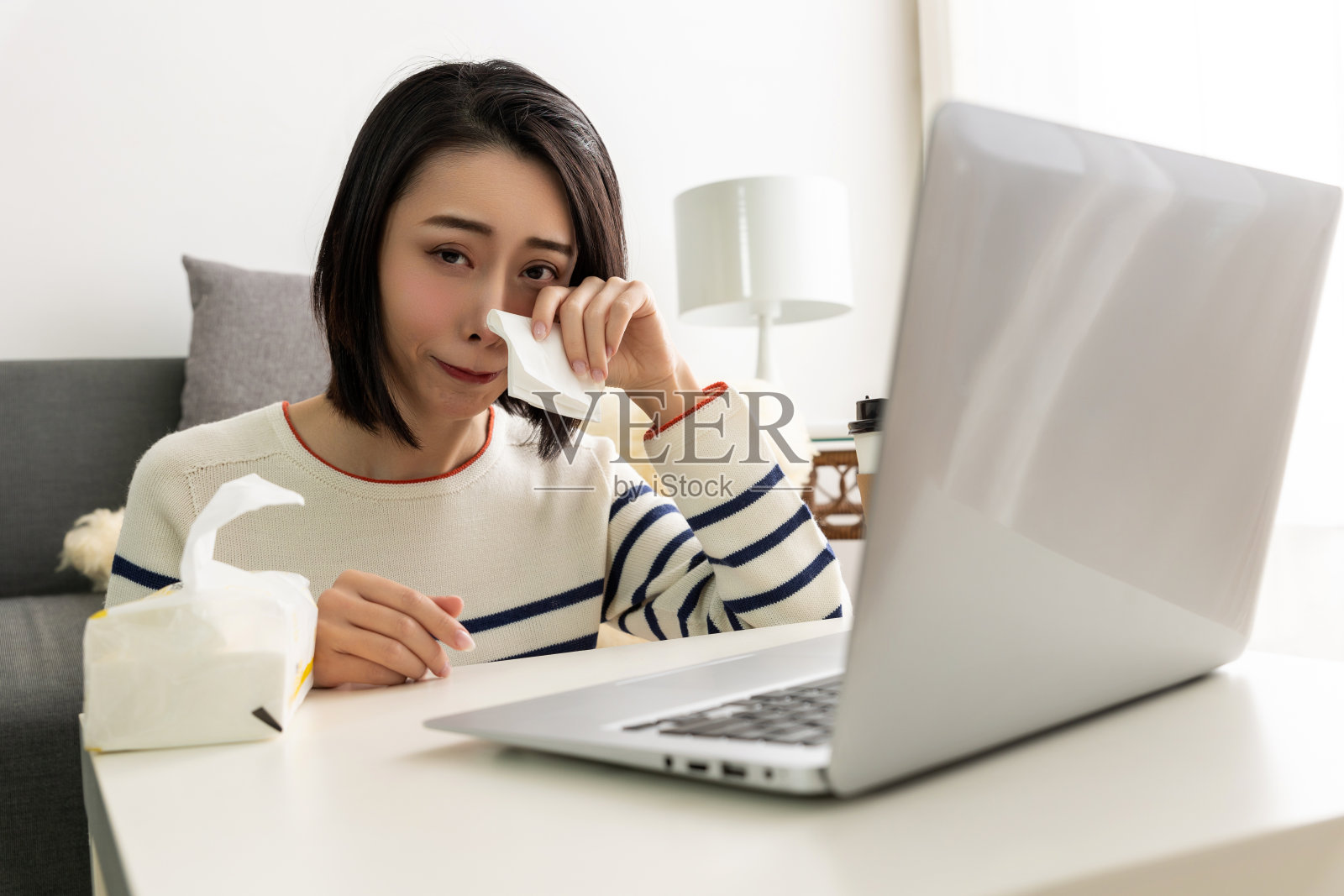 年轻漂亮的亚洲女人坐在客厅舒适的沙发上，同时使用她的笔记本电脑。照片摄影图片