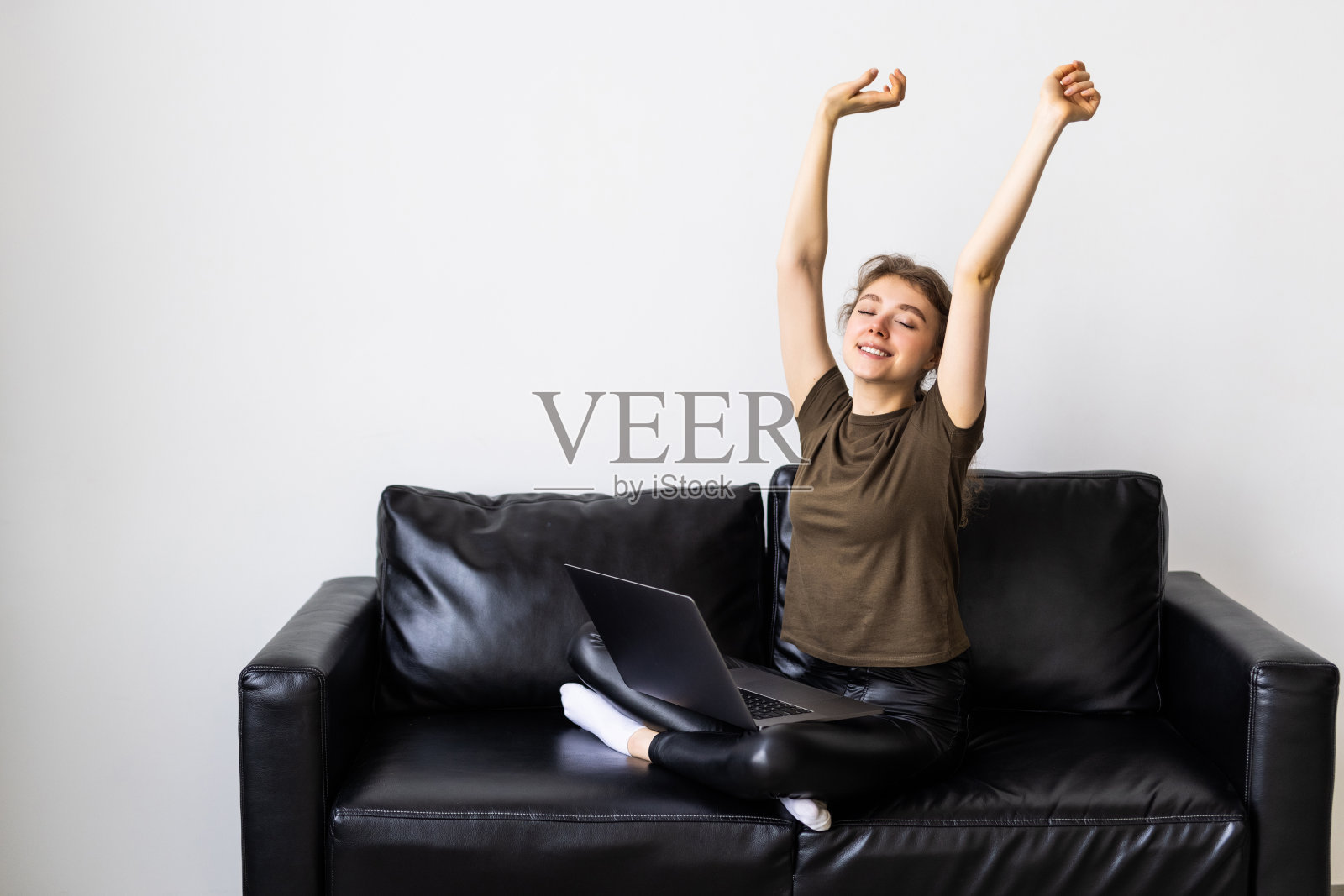 年轻的女商人在家工作，坐在沙发上伸展双臂，开心地微笑着照片摄影图片