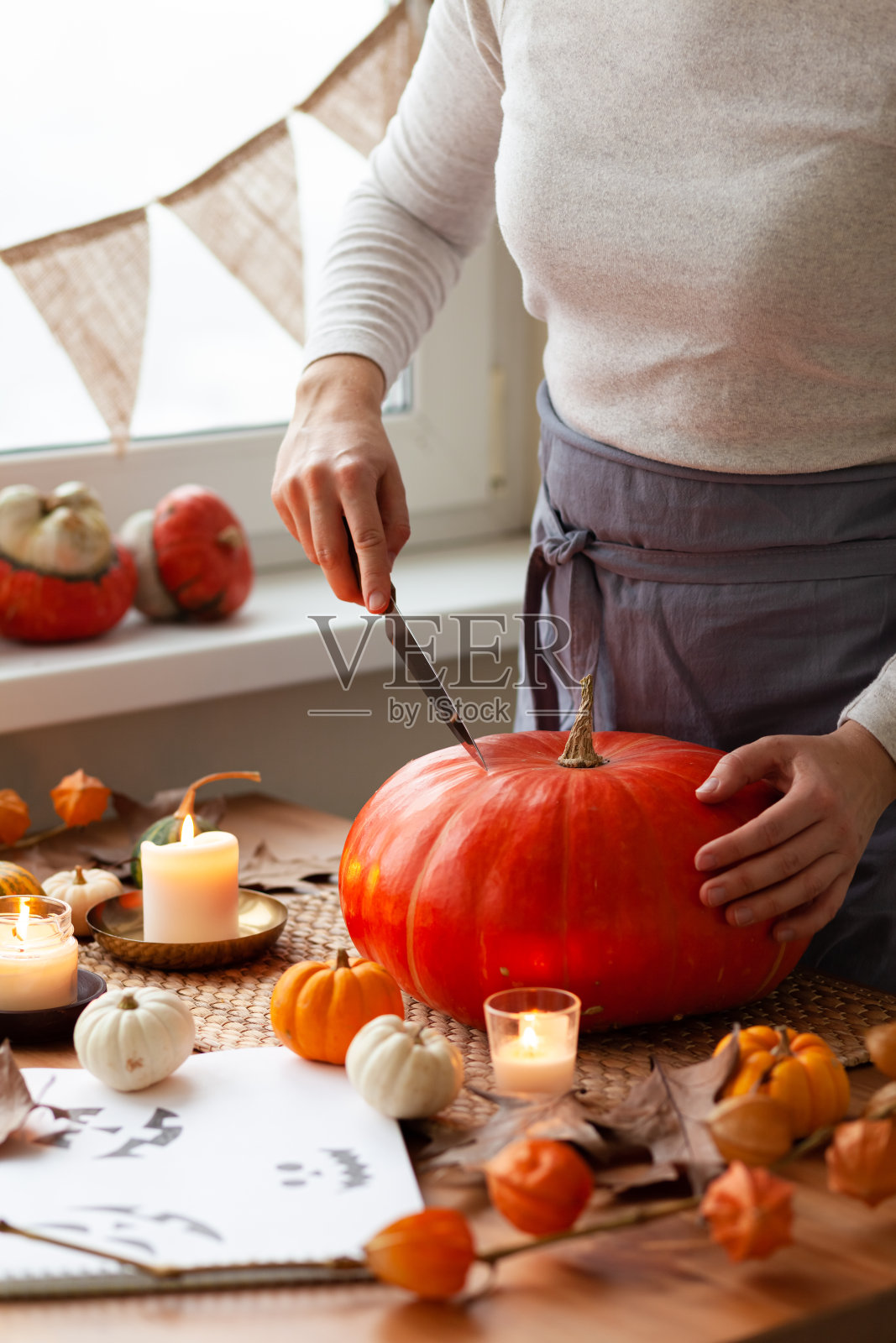 一名妇女在家里雕刻一个南瓜，用来手工制作杰克灯，作为万圣节派对的装饰。假日季节手工装饰概念。秋色，无脸，特写照片摄影图片