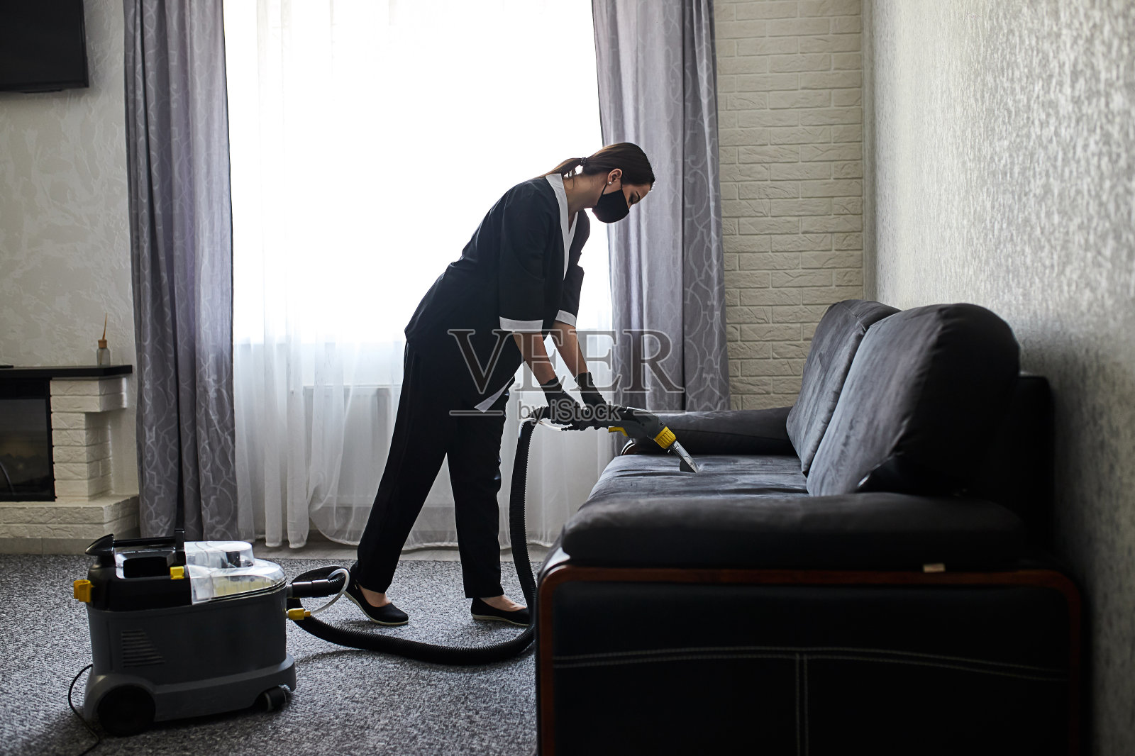 清洁服务公司员工用专业设备清除家具上的污垢。女管家手臂用吸尘器清洗沙发照片摄影图片