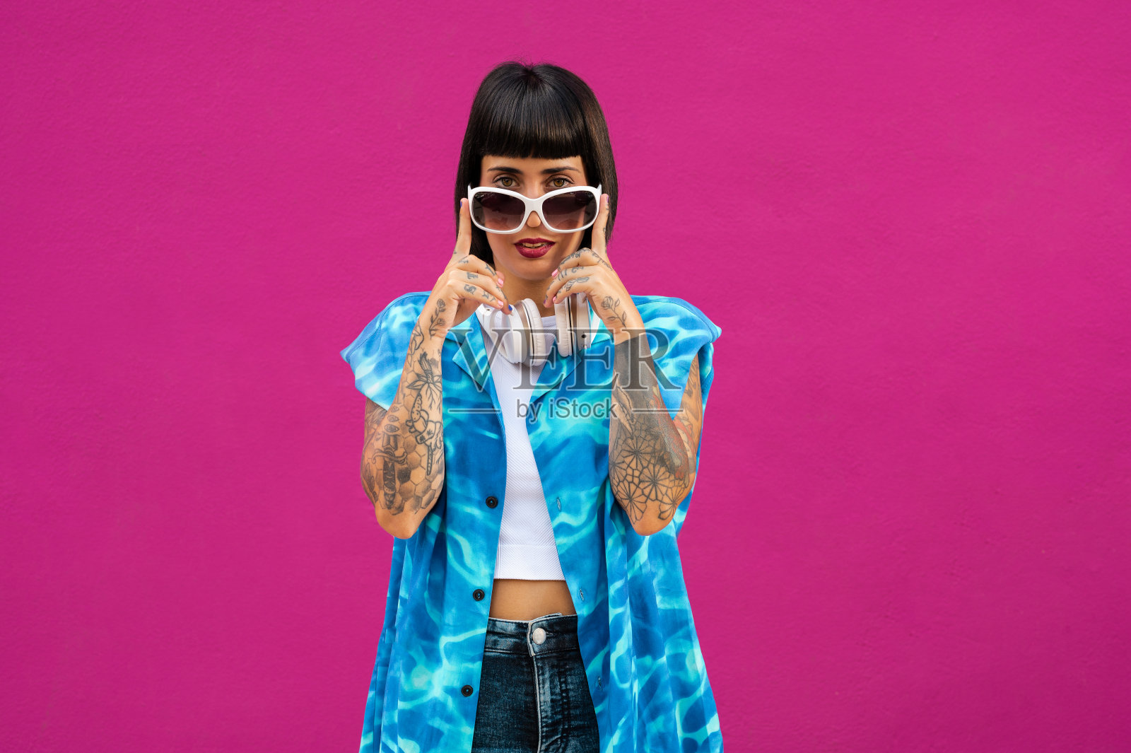 年轻的白人女性短发，手臂纹身，耳机在粉红色的背景照片摄影图片