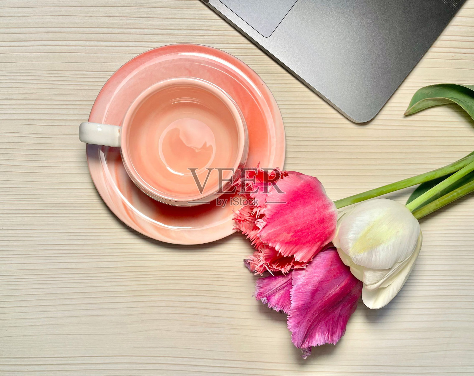 一个漂亮的粉色空咖啡杯摆在郁金香和笔记本电脑旁边照片摄影图片