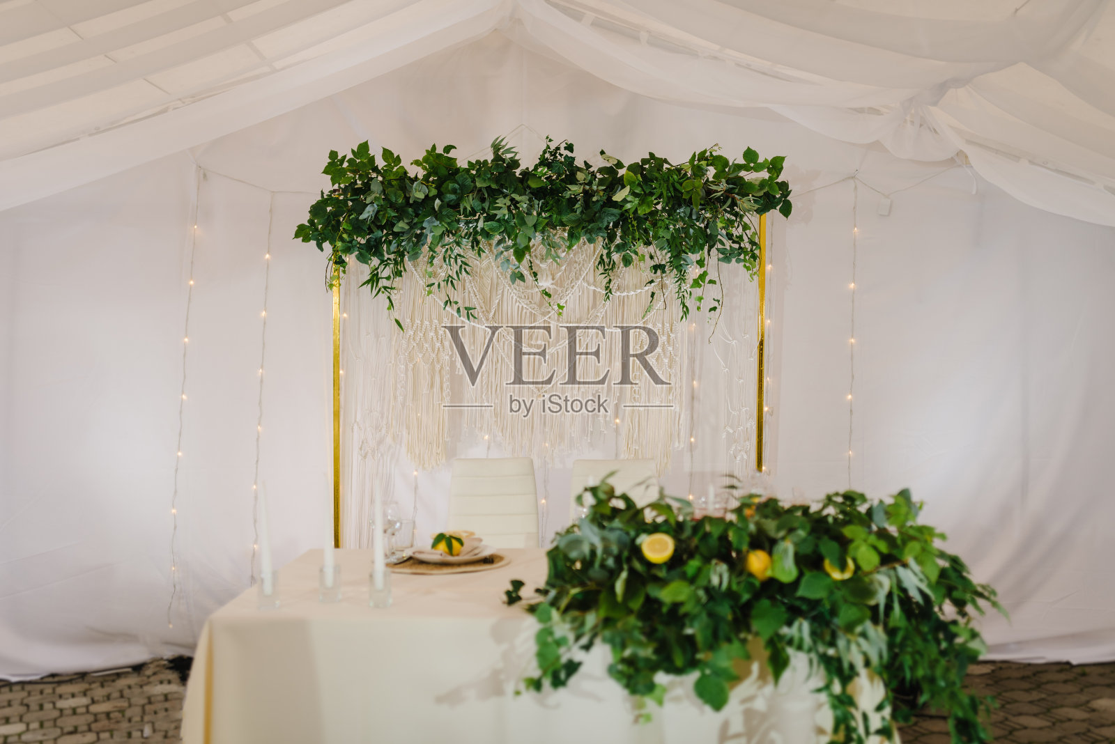 节日的桌子，拱门装饰树叶桉树绿色植物和花环与灯在帐篷。大厅里装饰着香草和柠檬。婚礼上新婚夫妇在宴会区豪华站立。准备仪式。照片摄影图片