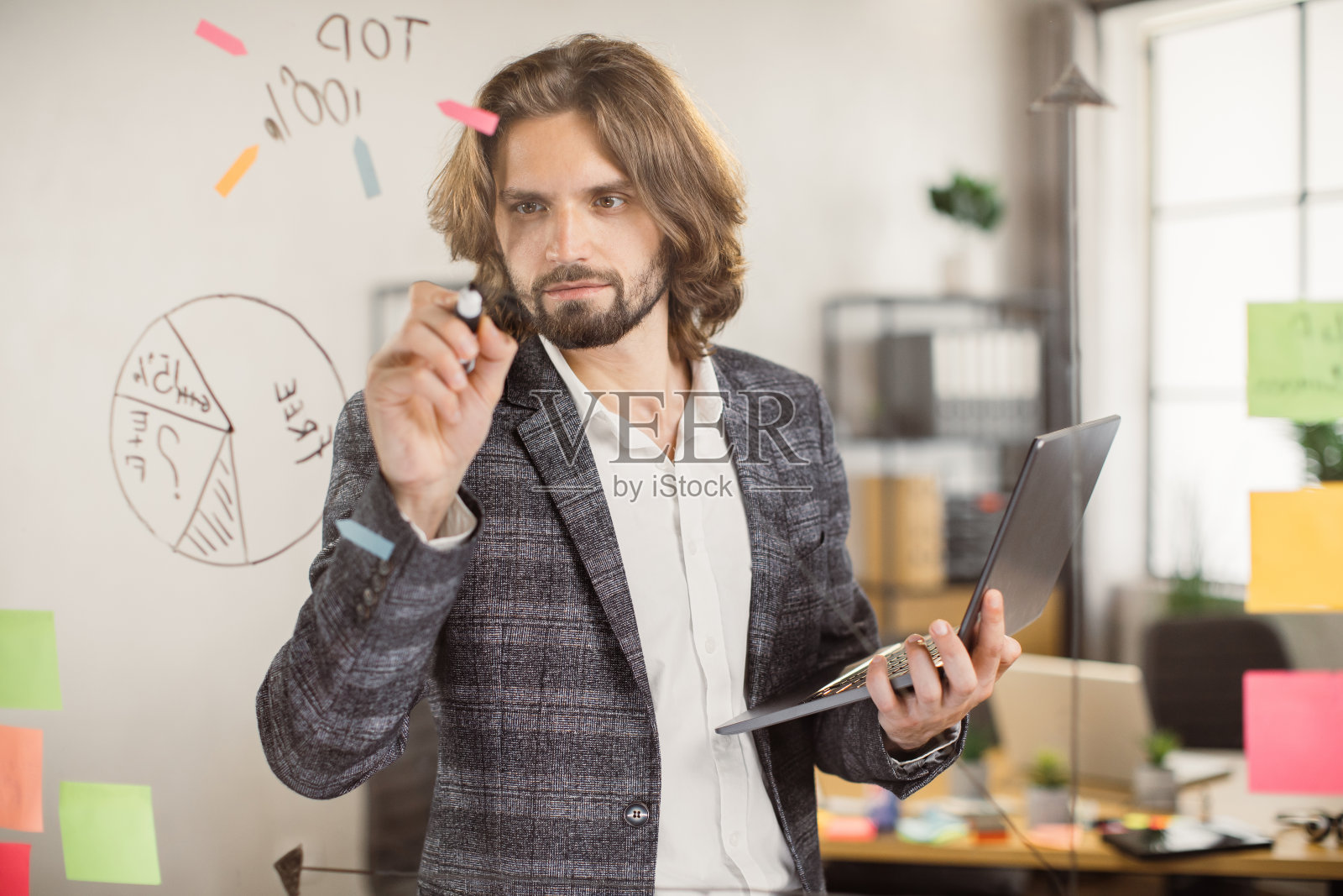 男员工在室内使用笔记本电脑，在玻璃板上写字照片摄影图片