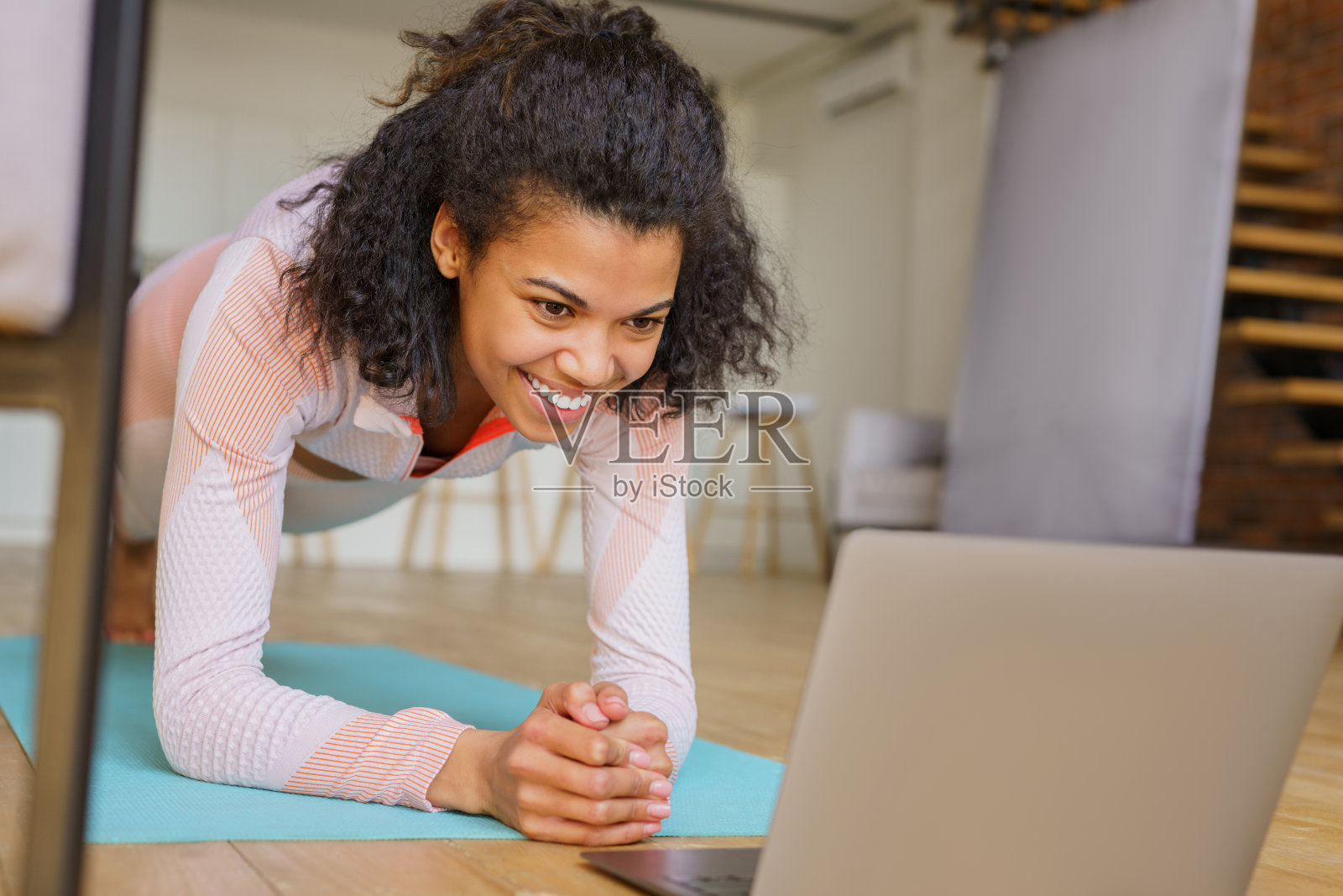 微笑的健身女子使用笔记本电脑观看在线教程，在家做平板支撑的站立练习。运动，健康的生活方式理念照片摄影图片