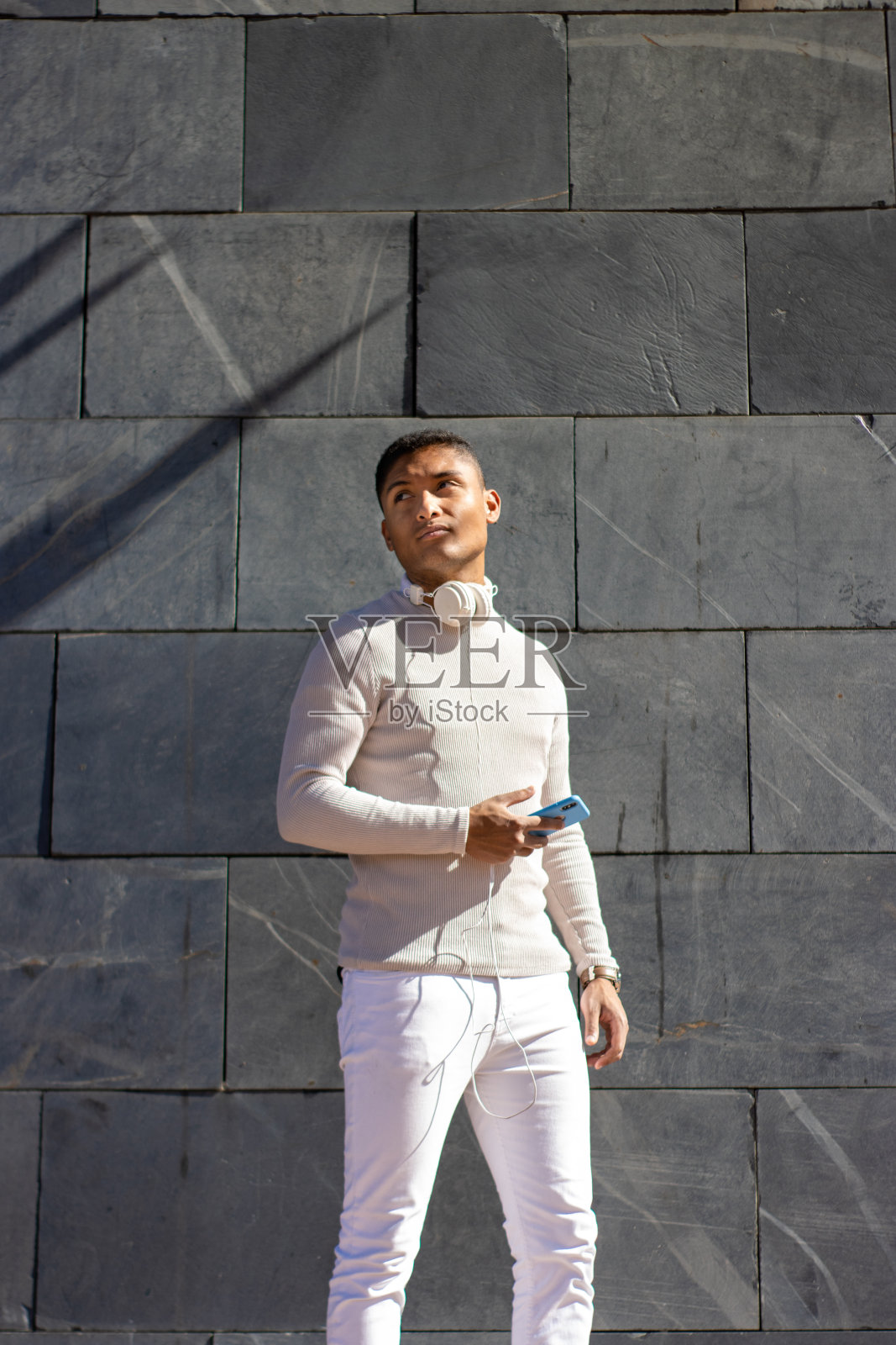 一名身穿白色衣服的男子，脖子上挂着耳机，手里拿着手机照片摄影图片