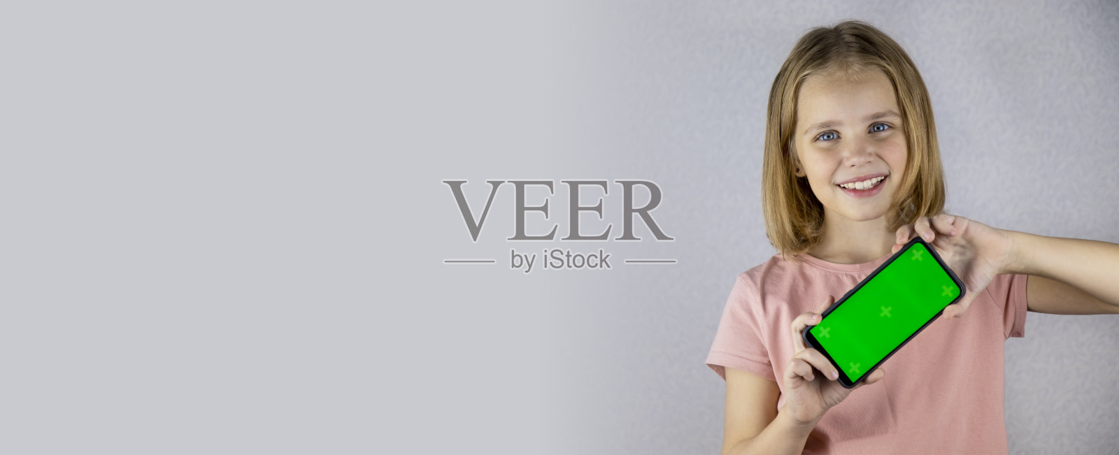 一位金发小女孩展示手中带有绿色屏幕的手机应用程序的肖像。他看着镜头，笑容满面。Banner照片摄影图片