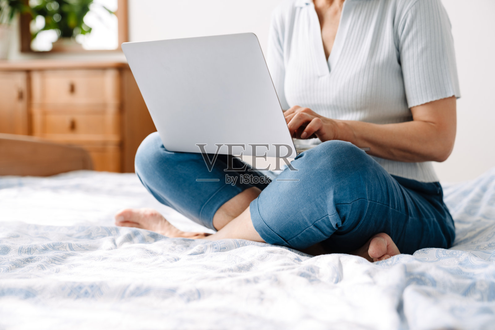 成熟的白色女性坐在床上用笔记本电脑打字照片摄影图片