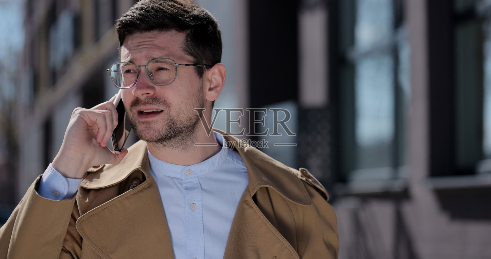 肖像帅哥戴着眼镜在街上打电话。商人在街上用智能手机聊天。户外，小玩意使用的概念。照片摄影图片