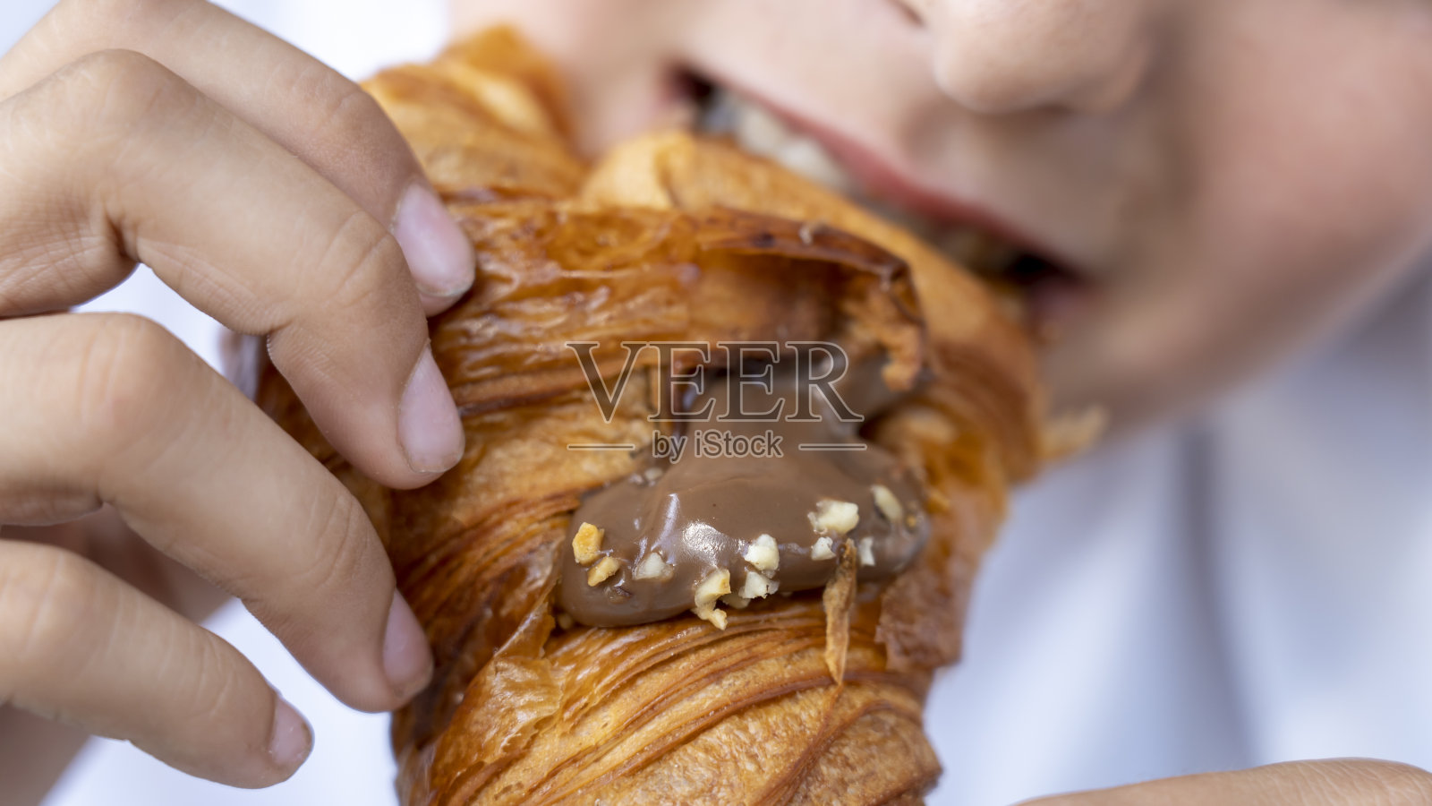 男孩吃了一个巧克力牛角面包。模糊的嘴。前景是巧克力奶油牛角面包。美味的甜食照片摄影图片