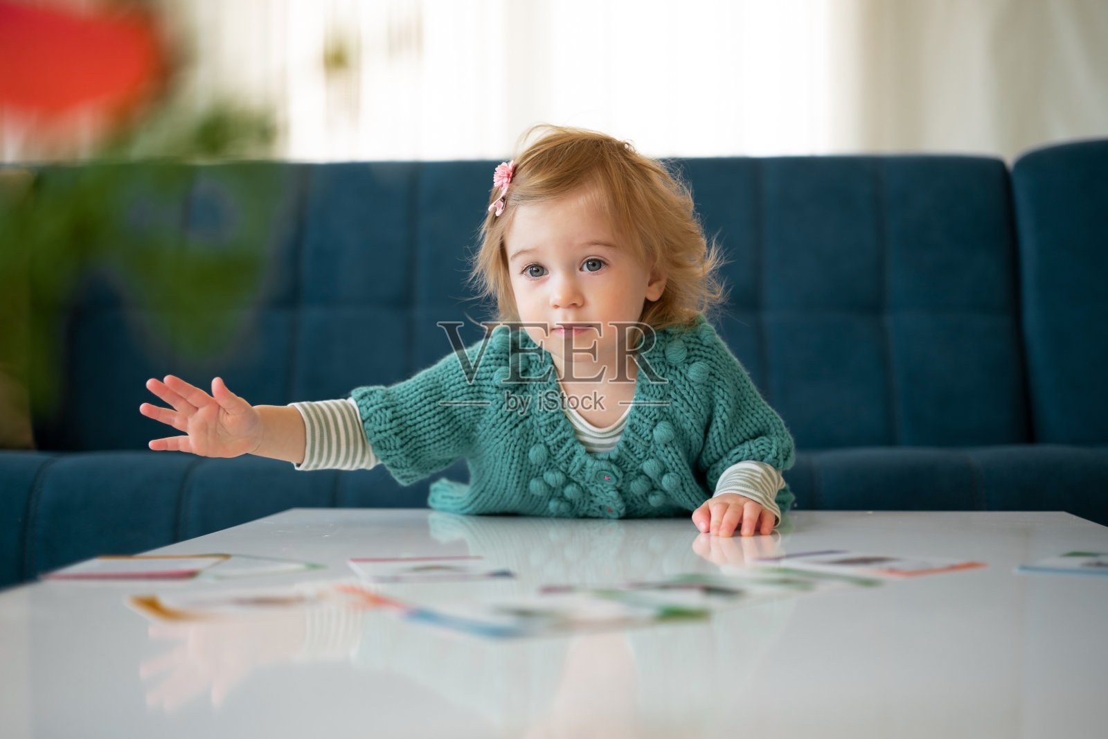 可爱的金发白种人小女孩1-2岁穿着毛衣在沙发的背景上玩卡片在现代室内在家里。孩子，婴儿，孩子花时间在室内生活方式照片摄影图片