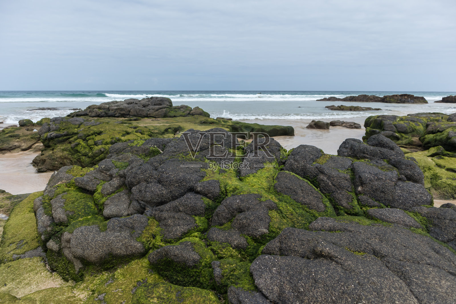 令人难以置信的沙滩上有黄色的沙子和带着海藻的黑色大岩石，天空中有大片灰色的云，大海在背景中拍打着海岸。Fuerteventura。加那利群岛。西班牙照片摄影图片