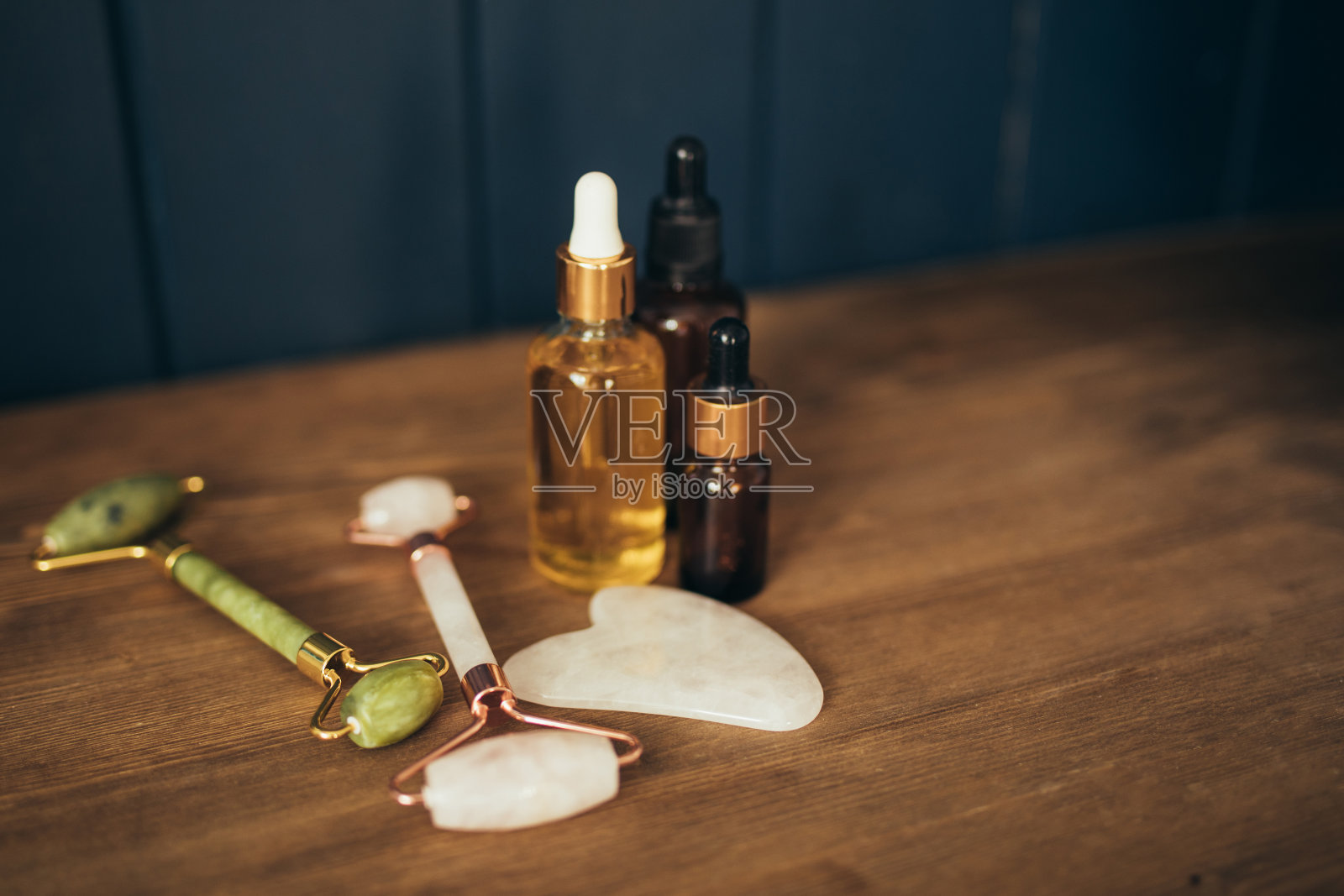 玉石滚轮和面部按摩器和天然油瓶子上的木制背景。皮肤护理。照片摄影图片
