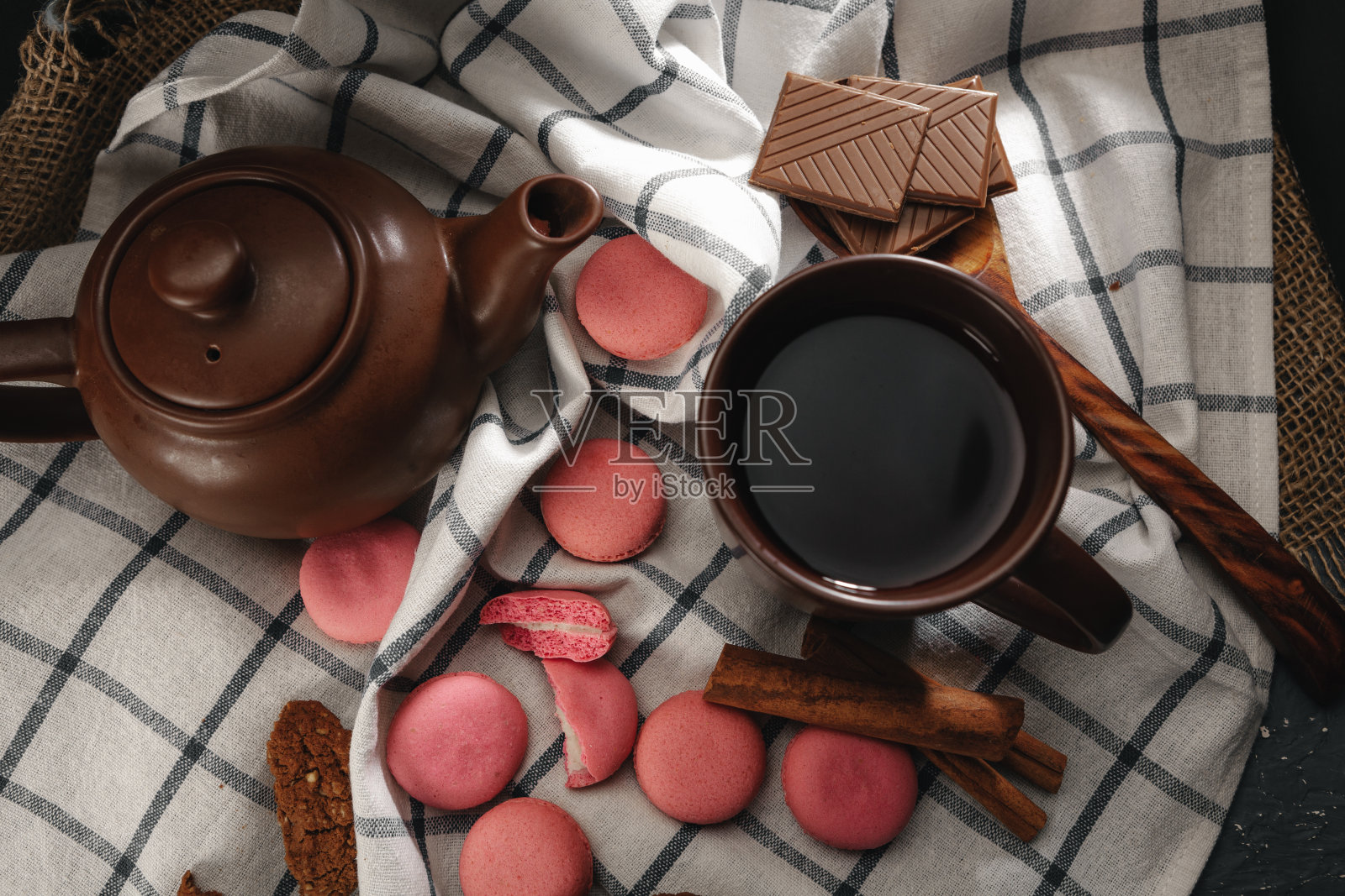 茶壶和茶杯放在厨房布上，点缀着粉红色的马卡龙照片摄影图片