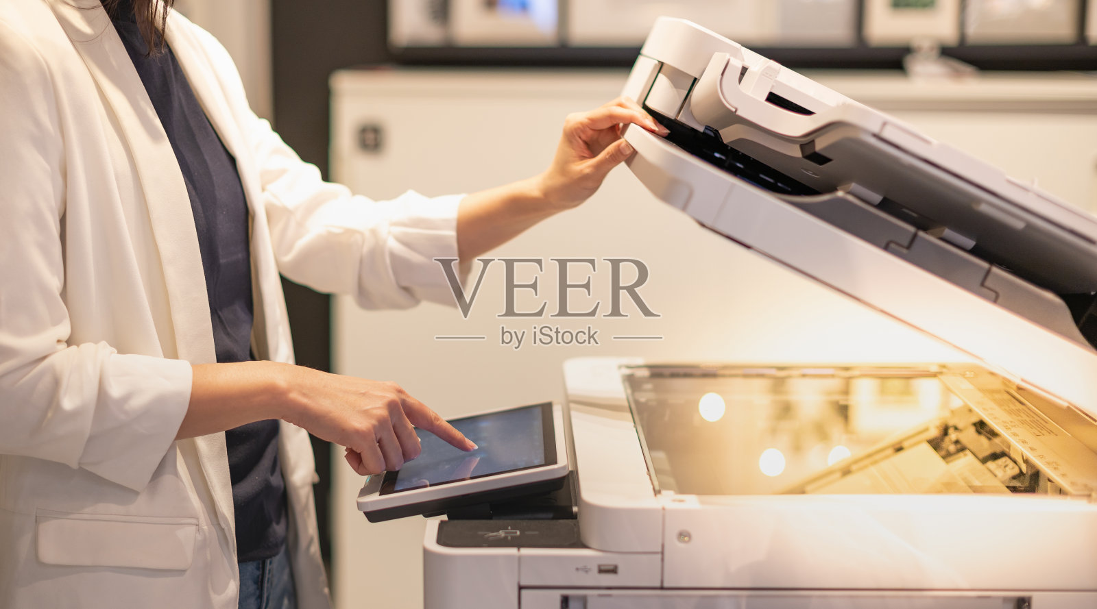 女职员站在办公室的复印机上，手按按钮。照片摄影图片