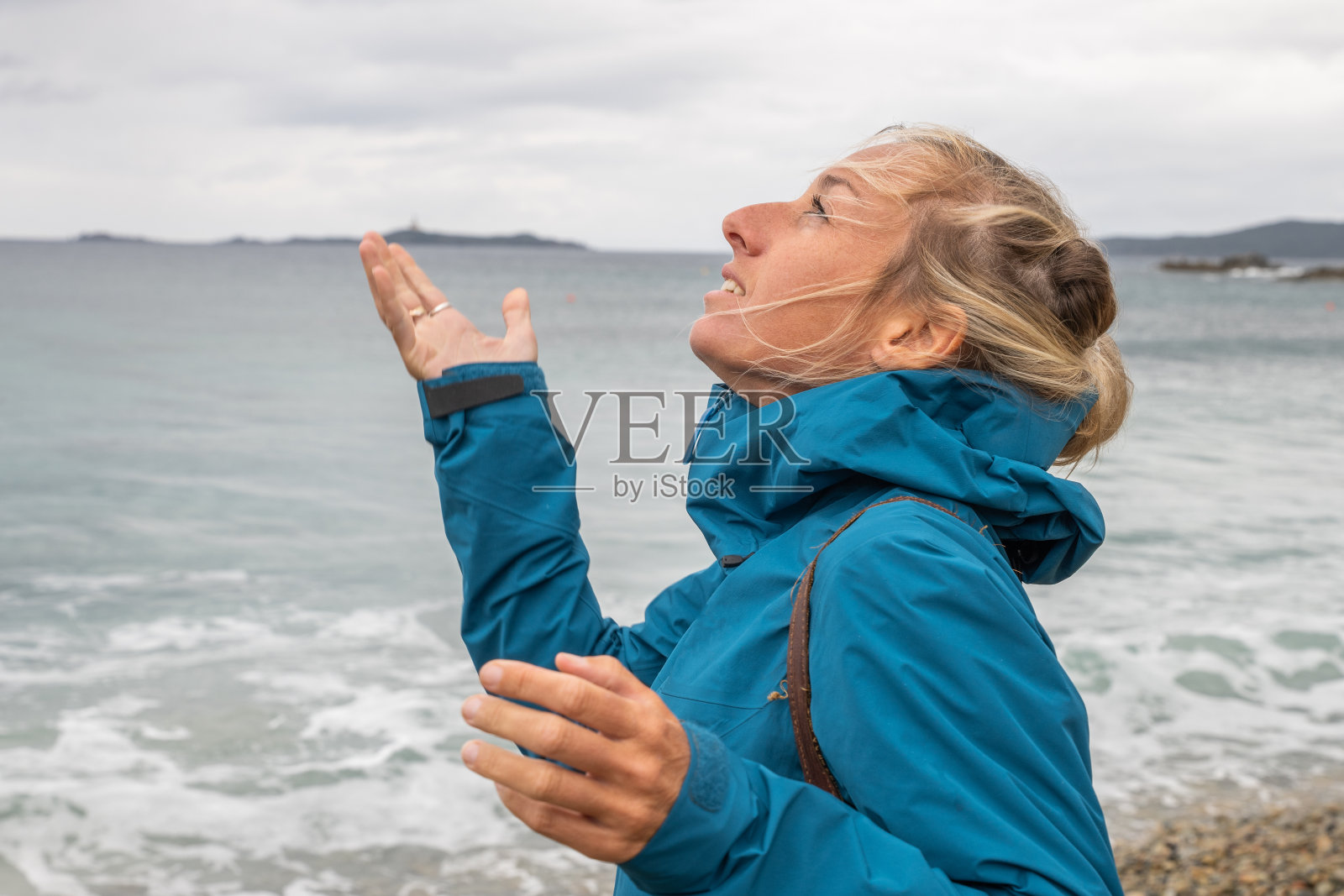 暴风雨天空下，在海滩上身穿雨衣仰望天空的年轻女子照片摄影图片
