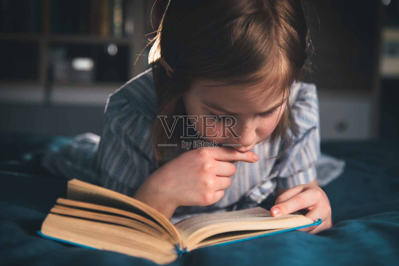 可爱的女孩在家里看书，躺在床上照片摄影图片