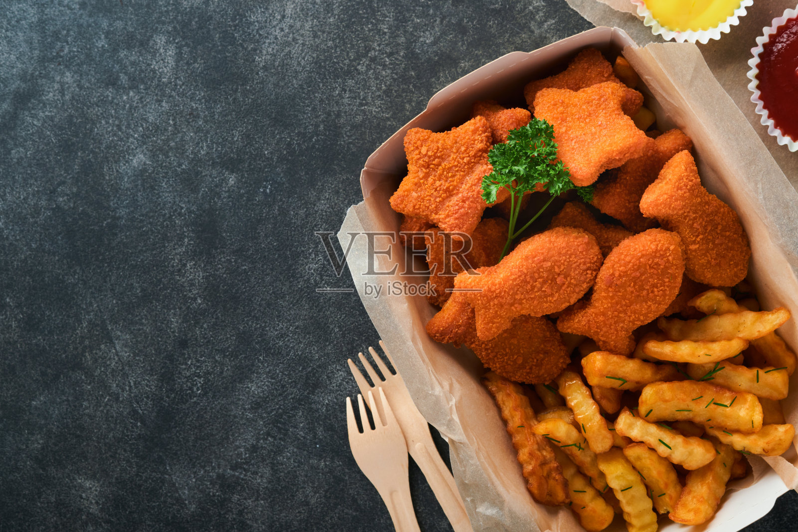 炸鱼薯条英国快餐。炸鱼条和薯条放在外卖纸盘上，黑色的旧混凝土背景。传统的英国正宗街头食品或外卖食品。模拟。照片摄影图片