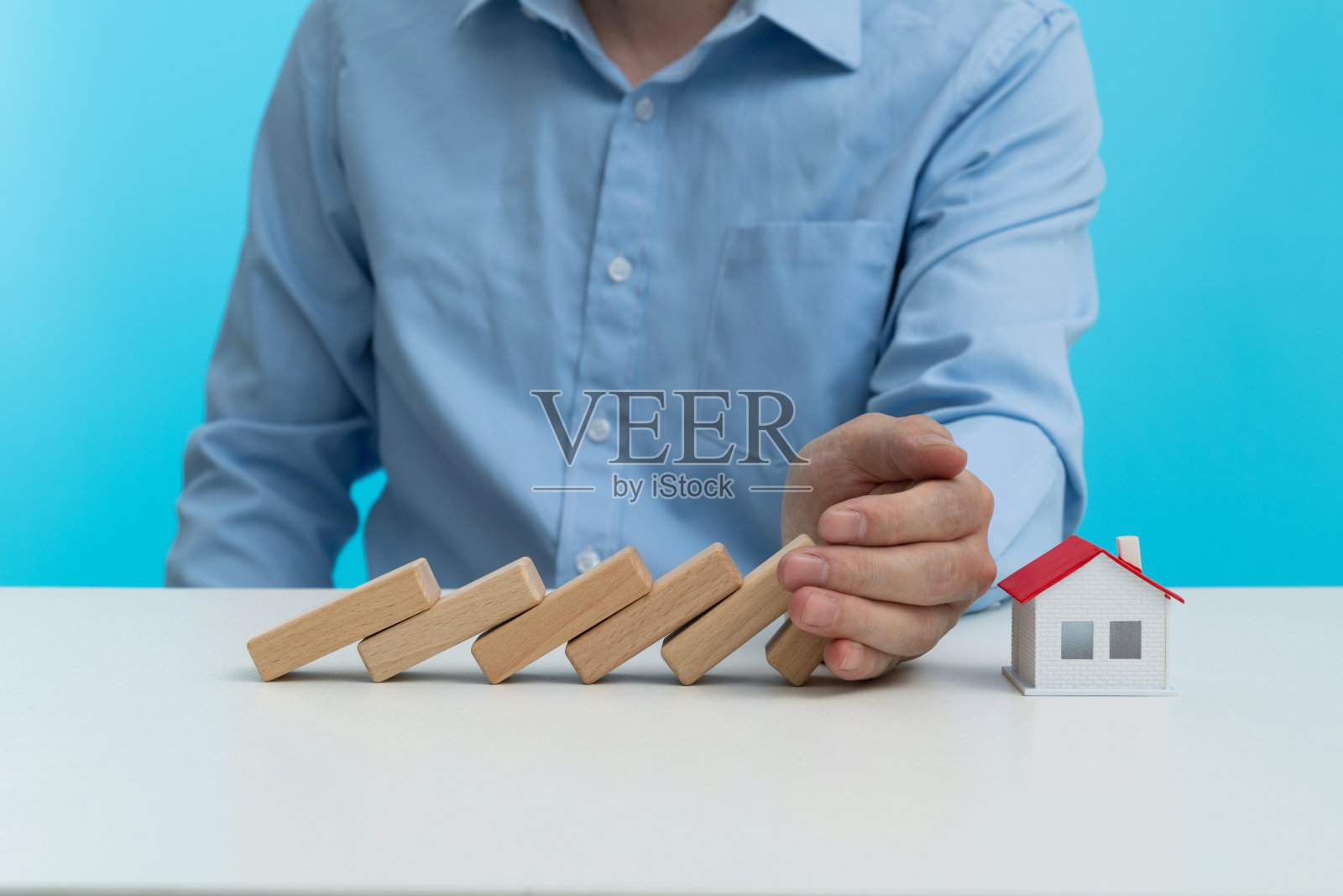 男人用手阻止多米诺骨牌掉在房子上照片摄影图片