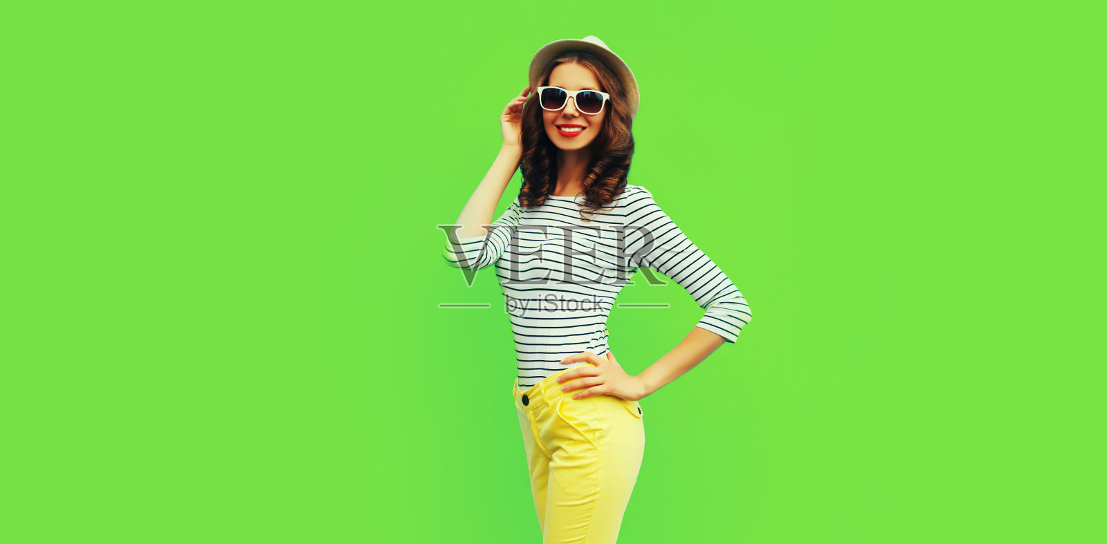 时尚微笑的年轻女性模特的肖像穿着条纹t恤和夏天的草帽在绿色的背景，空白的拷贝空间的广告文本照片摄影图片