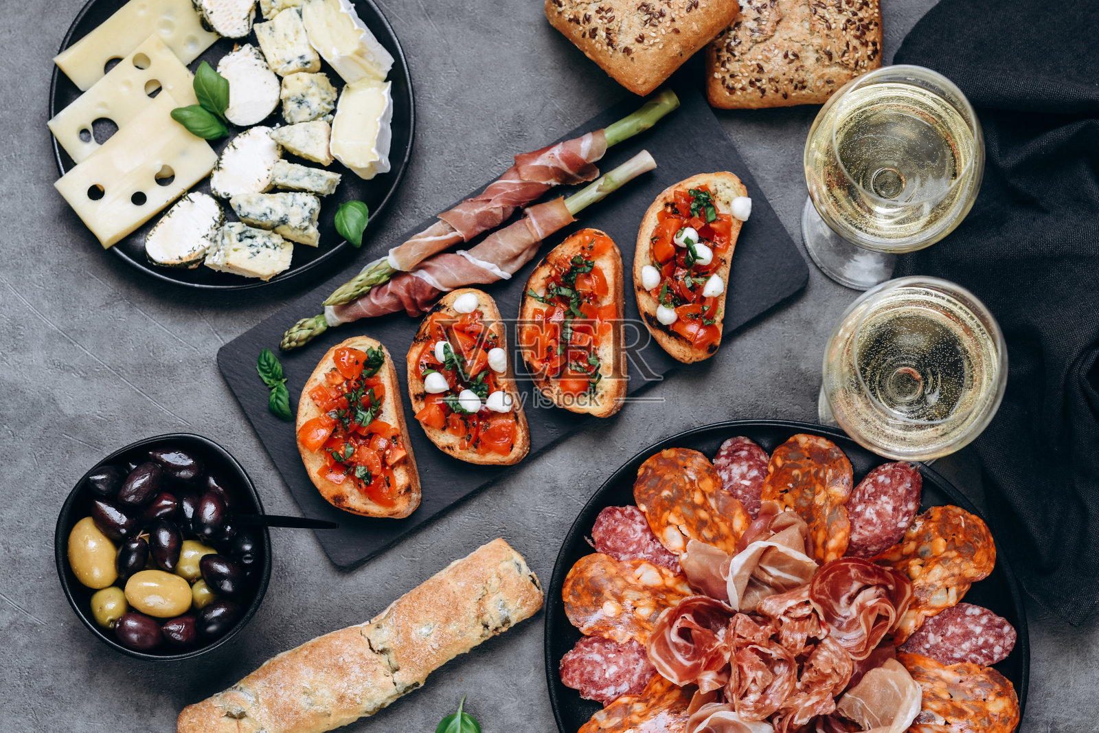 食物:意大利熏火腿，意大利腊肠，橄榄和面包，番茄罗勒烤面包板。两杯白葡萄酒或普罗塞克葡萄酒照片摄影图片